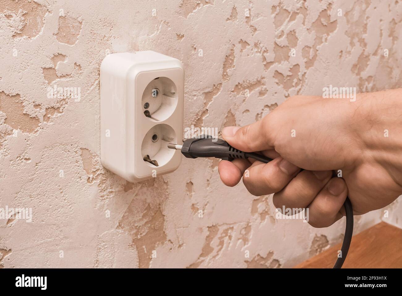 Ein Mann Hand legt oder entfernt einen Stecker aus einer Steckdose in einem modernen Interieur. Konzept für die sichere Verwendung von Elektrogeräten. Stockfoto Ein Mann Hand legt oder entfernt einen Stecker aus einer Steckdose in einem modernen Interieur. Konzept für die sichere Verwendung von Elektrogeräten. Stockfoto