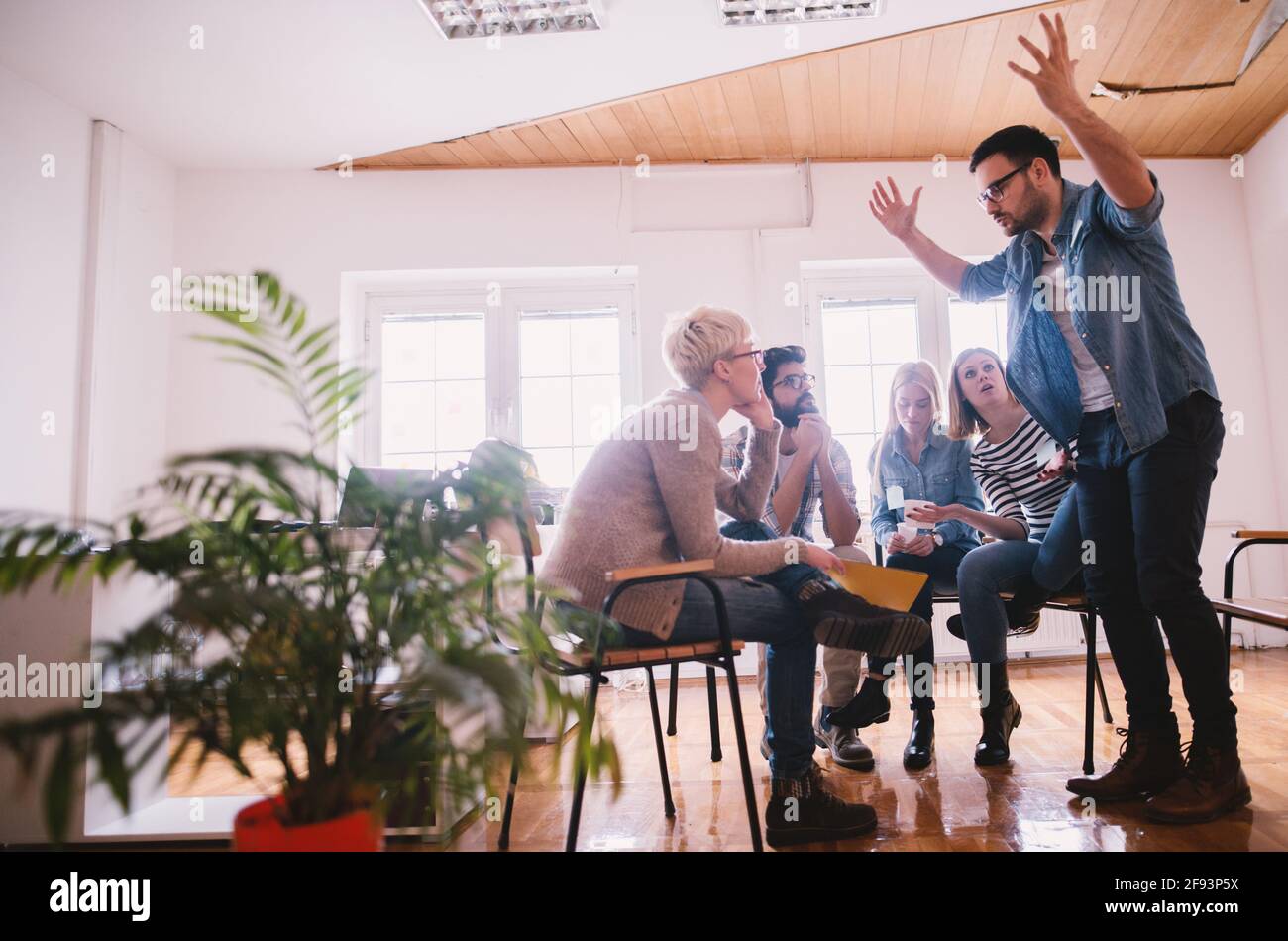 Junger verärgerter gutaussehender Kerl, der mit anderen Teilnehmern auf einer speziellen Gruppentherapie über seine gestresste Lebenssituation spricht. Stockfoto