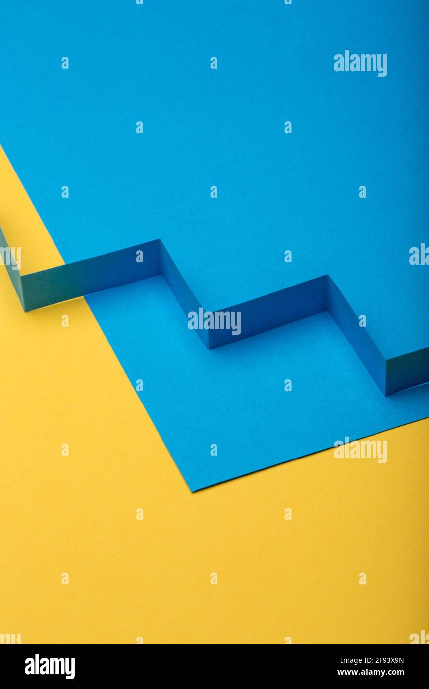 Abstrakter minimaler Papierhintergrund. Blaues Zick-Zack-Ausschneiden des Papierstreifens auf blauem und gelbem Papierhintergrund. Stockfoto