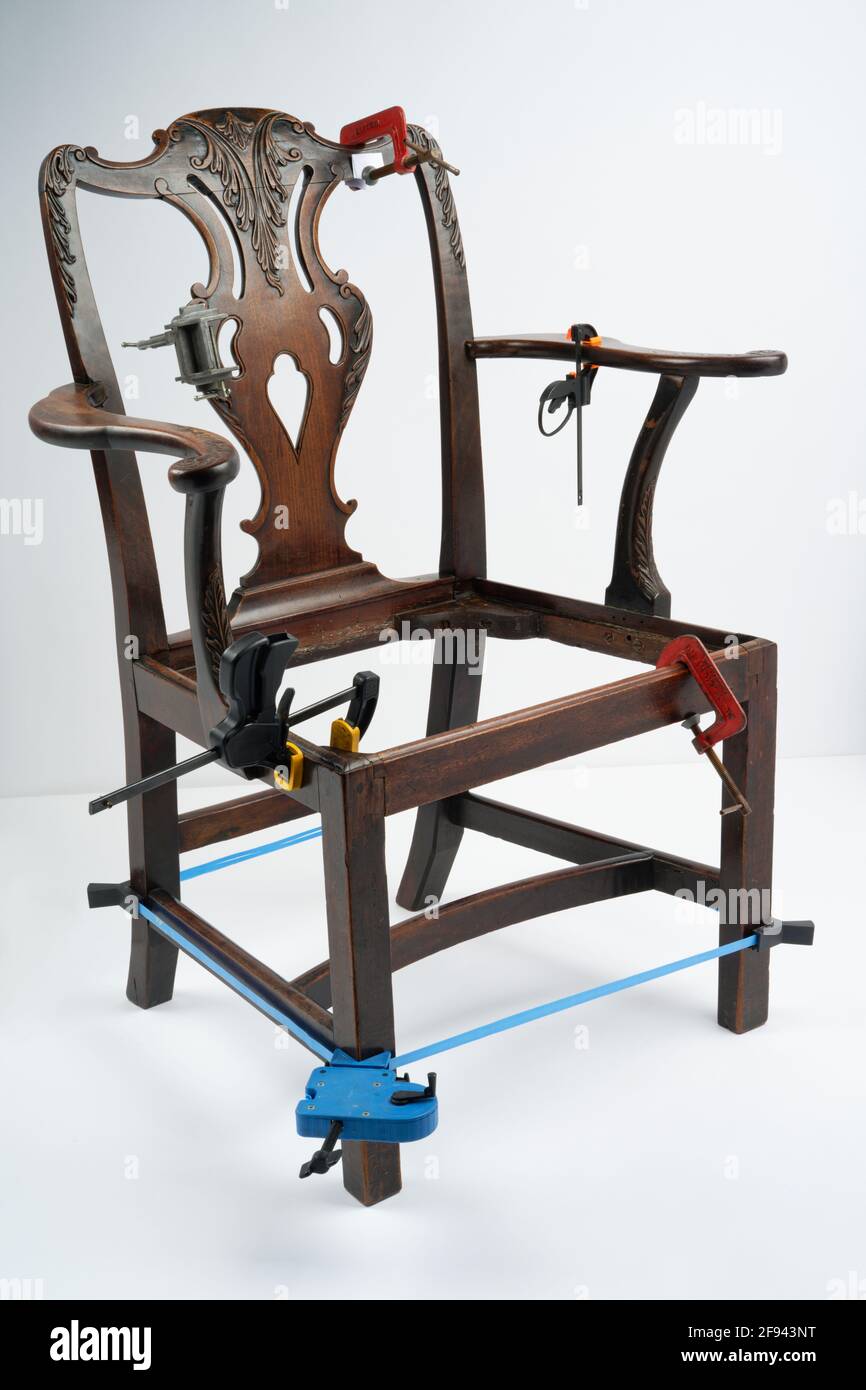 Reparatur oder Restaurierung eines antiken Stuhls auf weißem Hintergrund. Verschiedene Klammern halten den Holzrahmen zusammen. Stockfoto