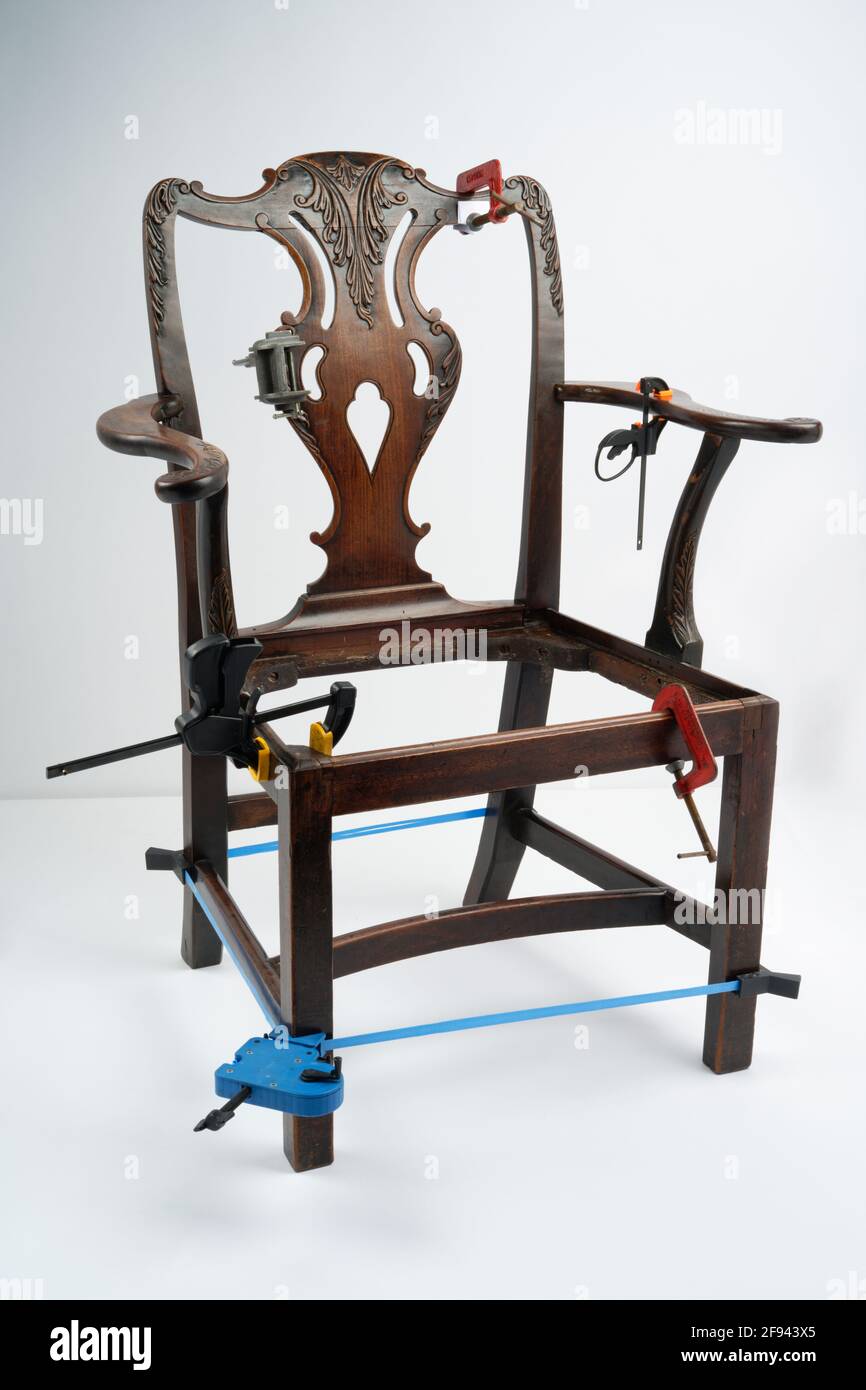 Reparatur oder Restaurierung eines antiken Stuhls auf weißem Hintergrund. Verschiedene Klammern halten den Holzrahmen zusammen. Stockfoto