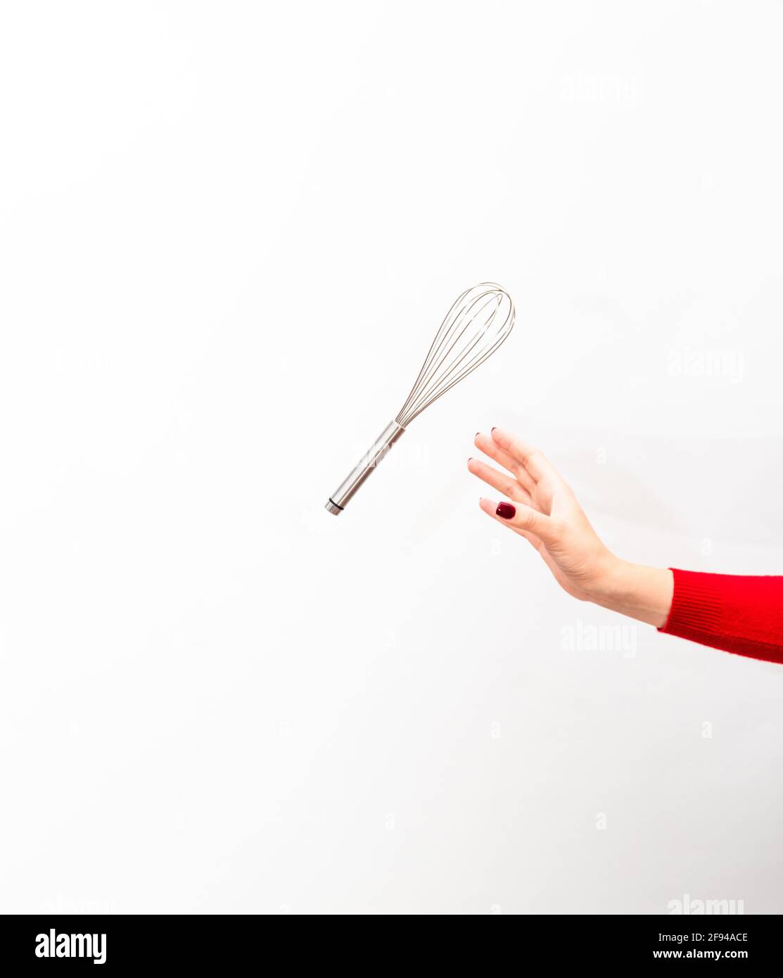 Eine Hand mit einer Maniküre fängt einen Schneebesen für die Nachspeise. Stockfoto