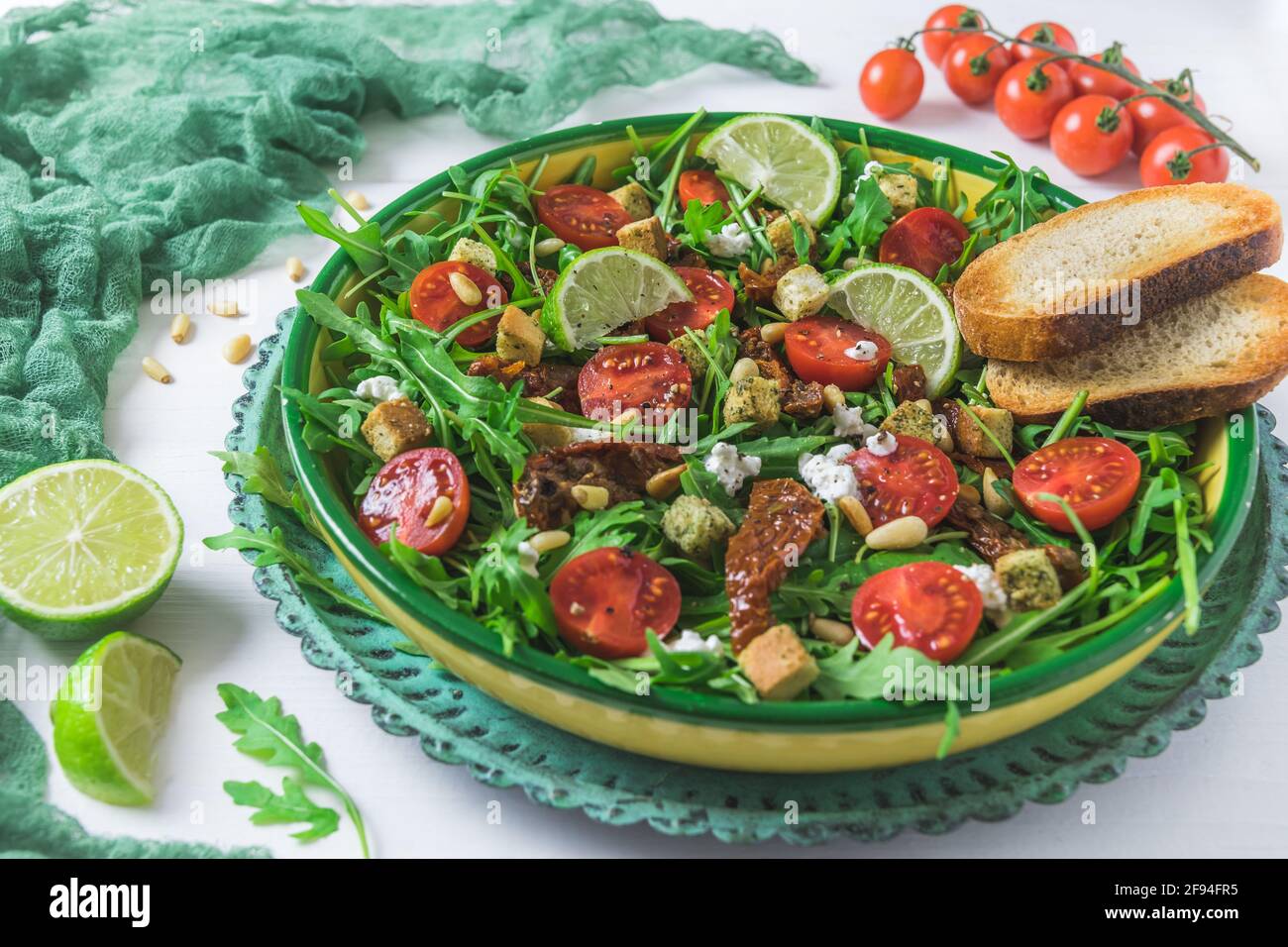 Schüssel mit frischem Gemüsesalat: Rucola, frische und getrocknete Kirschtomaten, Pinienkerne und Käse auf weißem Holzhintergrund Stockfoto