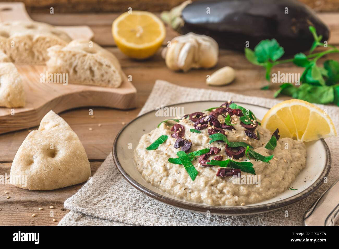 Arabische Küche: Baba Ganoush mit schwarzen Oliven und gehackter Petersilie und Fladenbrot auf einem rustikalen Holztisch Stockfoto