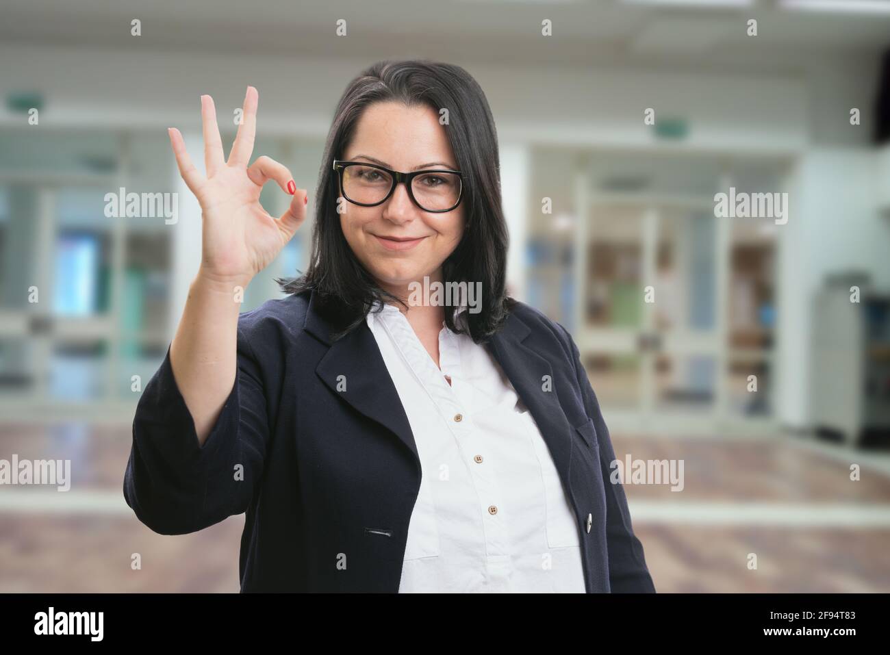 Geschäftsfrau mit freundlichem Lächeln in elegantem, legerem Büroanzug Eine gute Geste im Gebäude als Hintergrund Stockfoto
