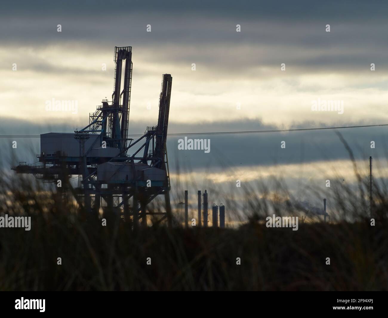 Zwei mächtige Kraniche in der Teesport Container Facility in schlichtem Silhouette und Dinosaurierähnlich, vor einem leuchtenden, wolkengestreiften Winterhimmel. Stockfoto