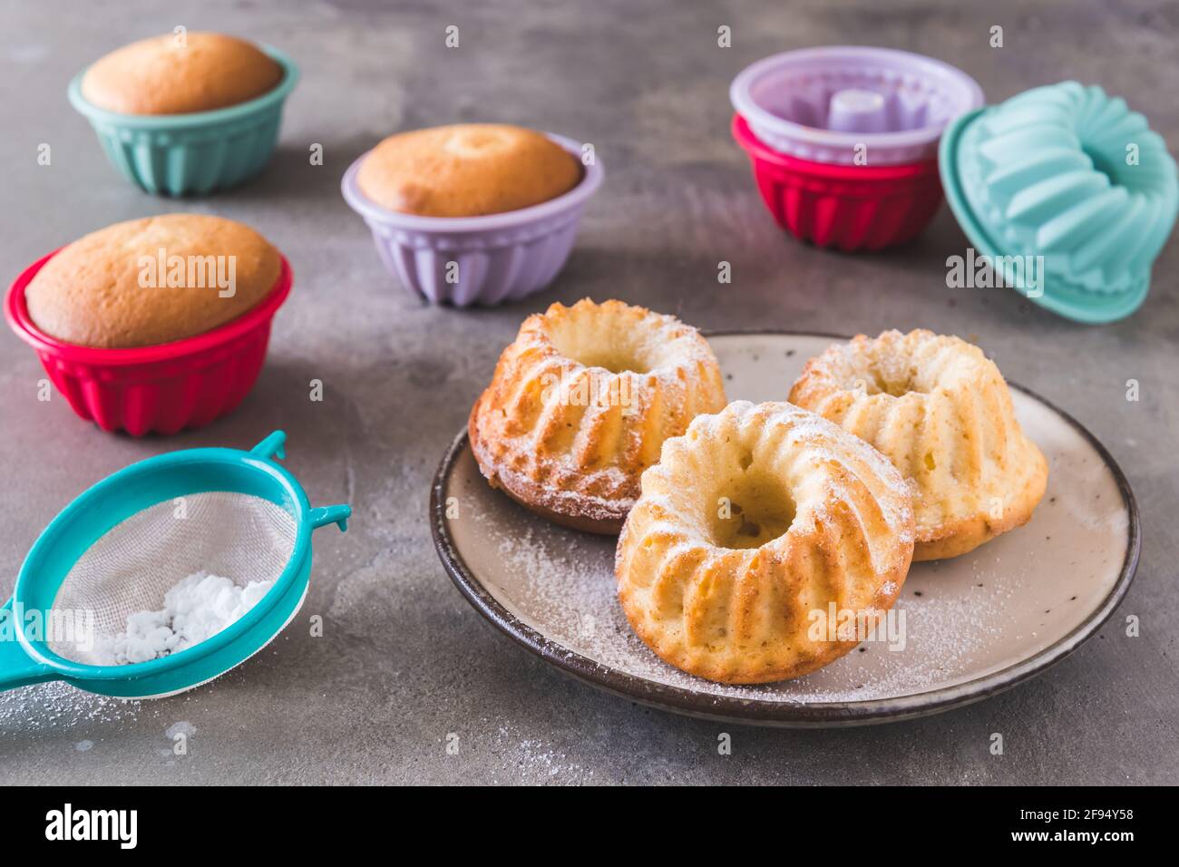 Hausgemachte Mini-Bunt-Kuchen und ihre bunten Silikon-Kuchenformen Auf grauem Hintergrund Stockfoto