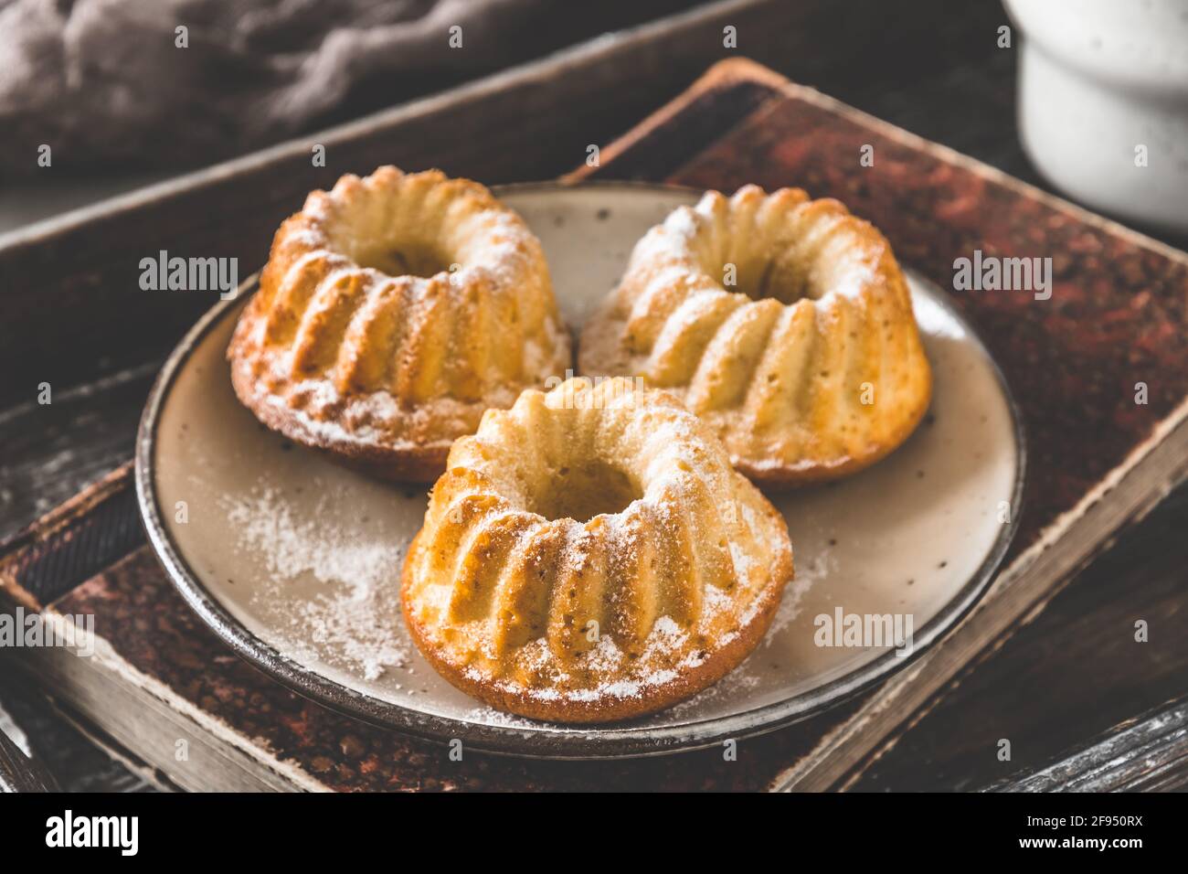Drei Mini-Bündelkuchen auf einem Teller und ein alter Buch auf einem Holztablett auf grauem Hintergrund Stockfoto