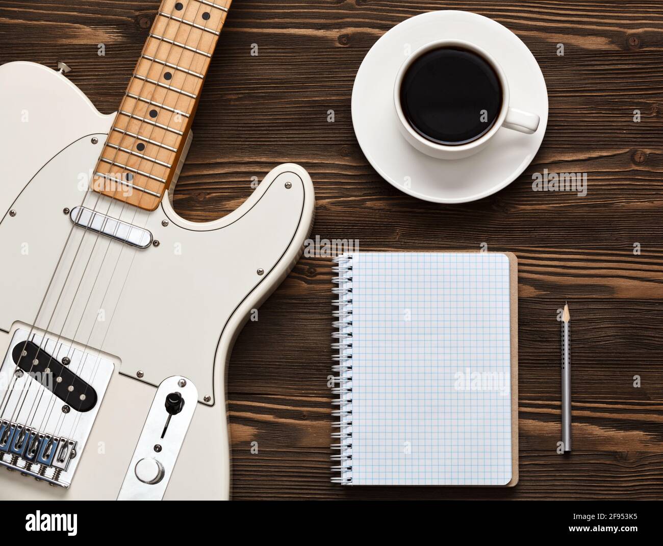 Eine Tasse Kaffee, eine Gitarre und ein Notizbuch auf einem dunklen Holzbrett. Stockfoto