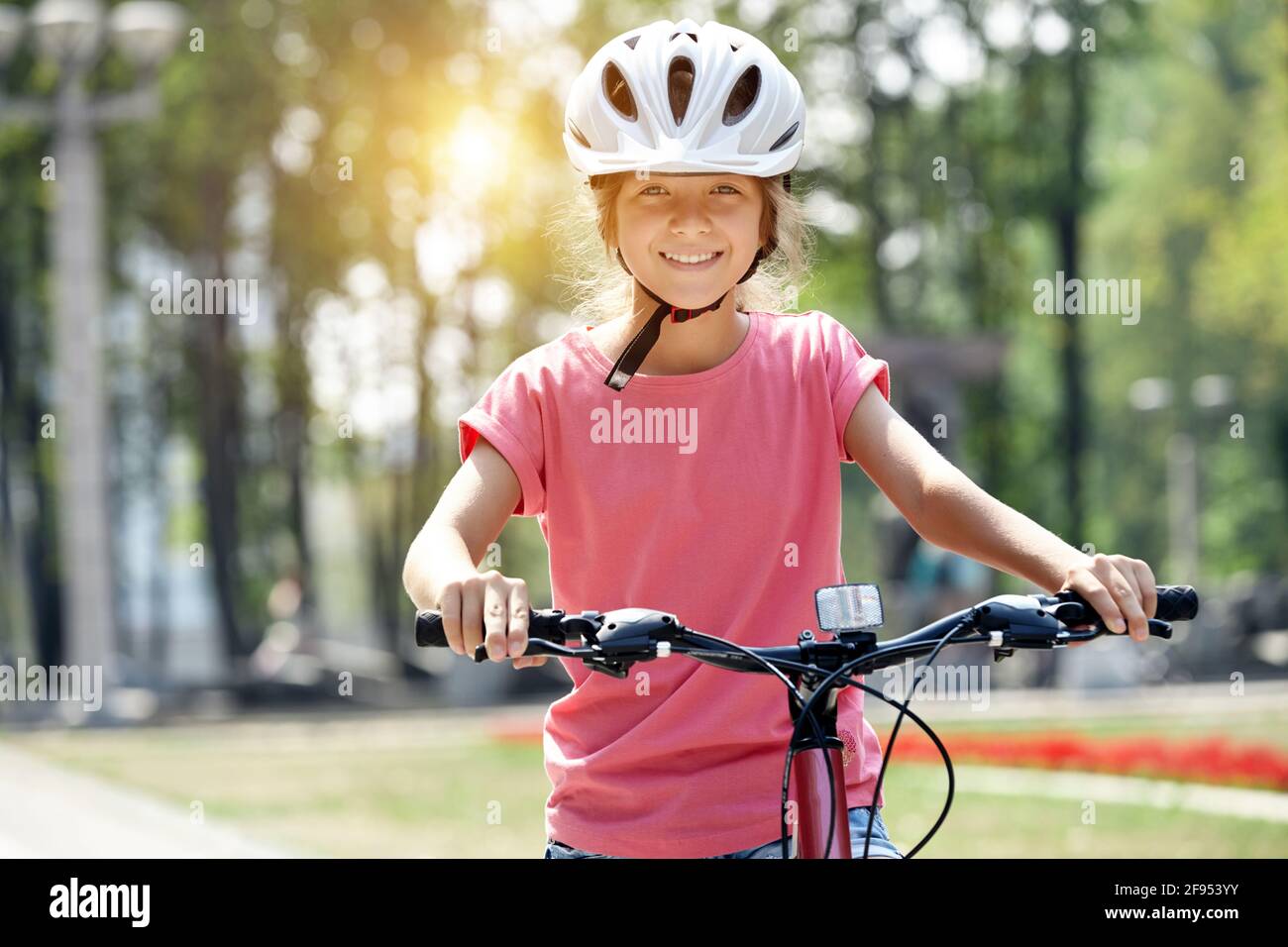 Mädchen mit Helm und Fahrrad im Stadtpark. Schaut auf die Kamera und lächelt. Stockfoto