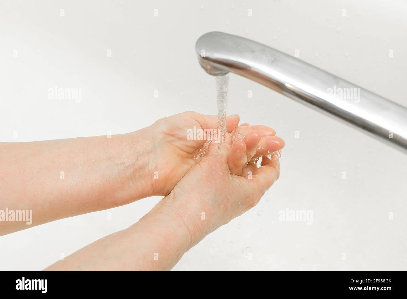 Eine ältere Frau wäscht ihre Hände unter fließendem Wasser im Badezimmer. Haushaltshygiene. Stockfoto