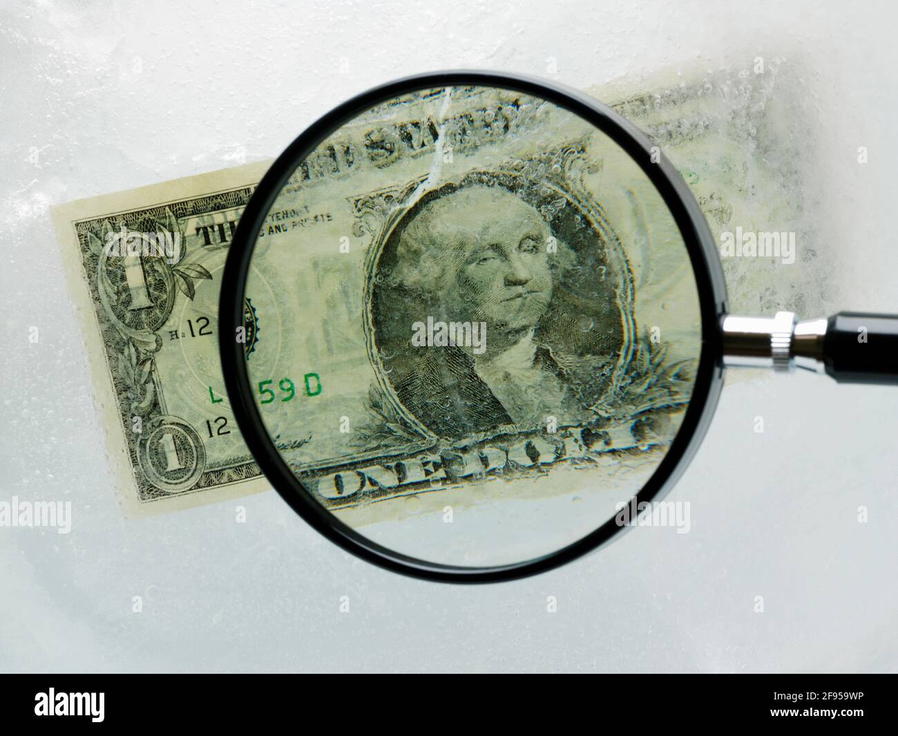 Der amerikanische Dollar-Schein ist in Eis gehüllt und wird durch eine Lupe betrachtet Glas Stockfoto