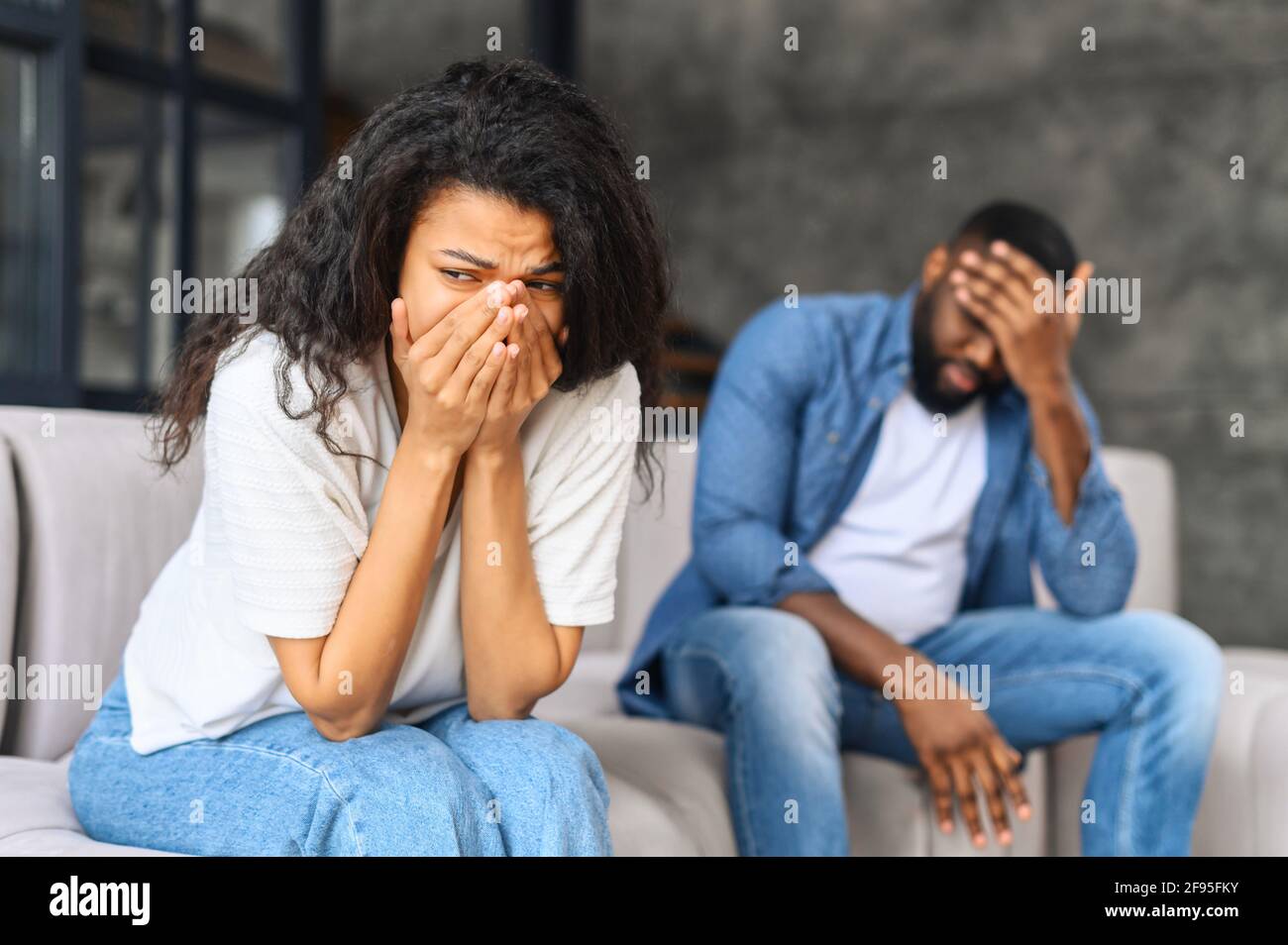 Junge biracial Paar Beziehung Problem Konzept, afrikanische Frau traurig und weinend nach haben einen Streit zu Hause, traurig oder deprimiert Frau sitzt auf dem Sofa mit ihrem Paar, Mann in Unschärfe sitzt in der Nähe Stockfoto