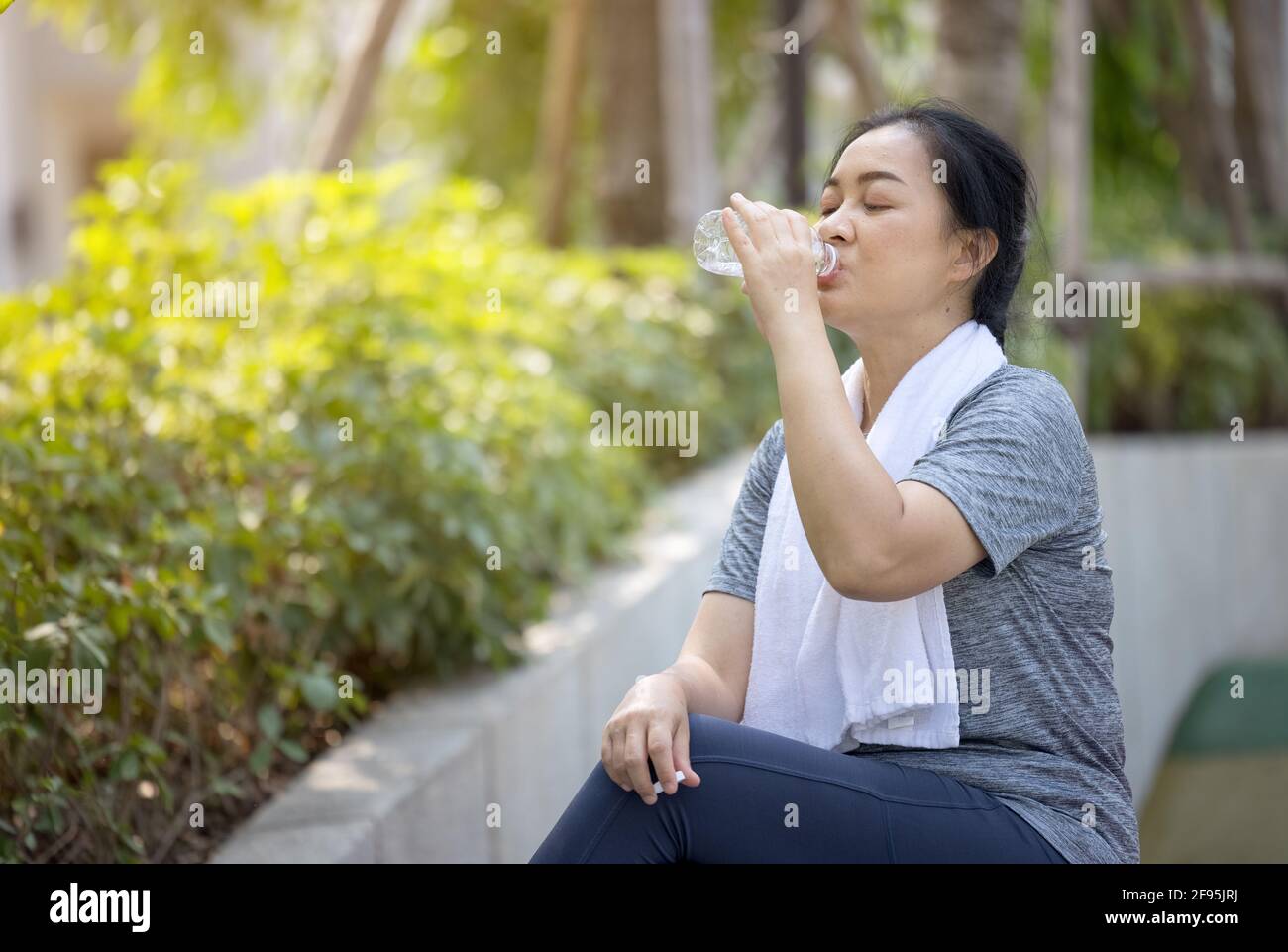 Eine ältere sportliche Frau trinkt Wasser aus einer Flasche, nachdem sie im Park gelaufen ist. Stockfoto