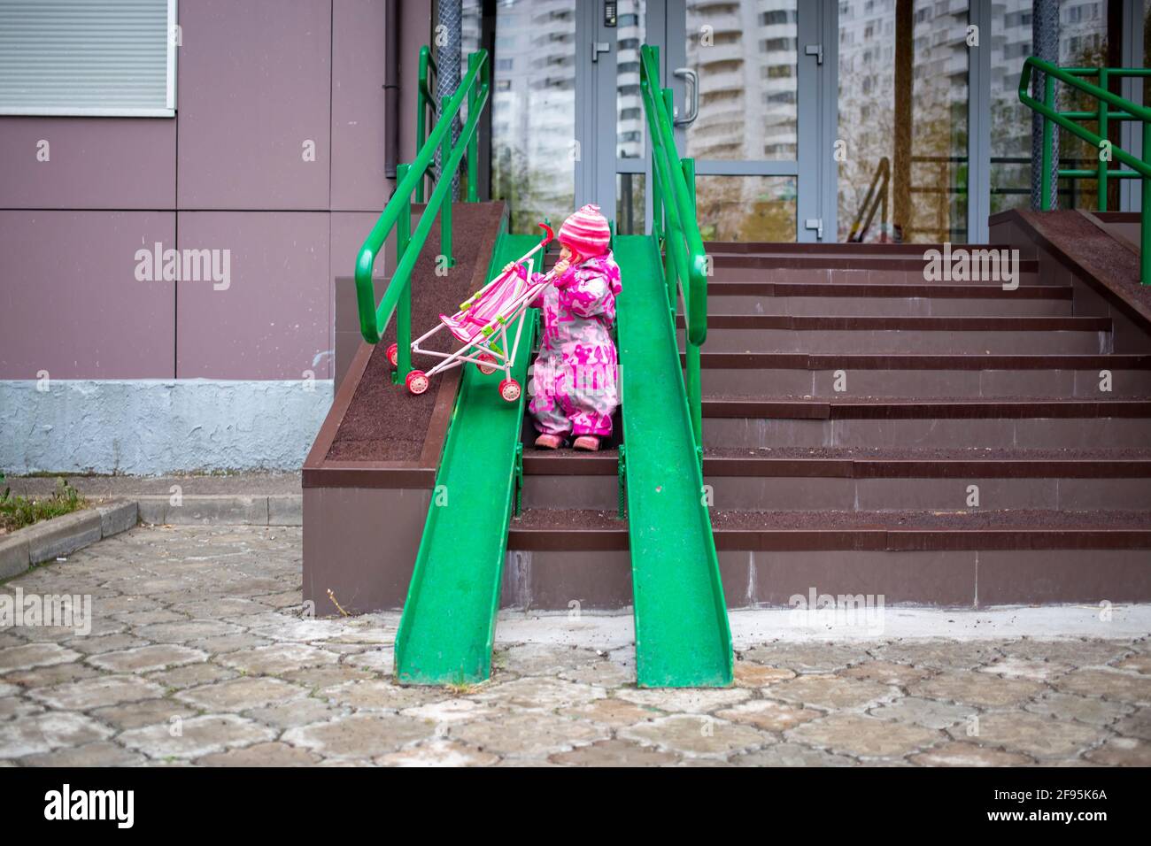 Nettes Kleinkind mit einem Spielzeug Kinderwagen geht entlang Stahl  Gelnder Rampe fr Rollstuhl, Wagen und Kinderwagen. Sanfte Abstieg von der  Treppe im Freien Stockfotografie - Alamy