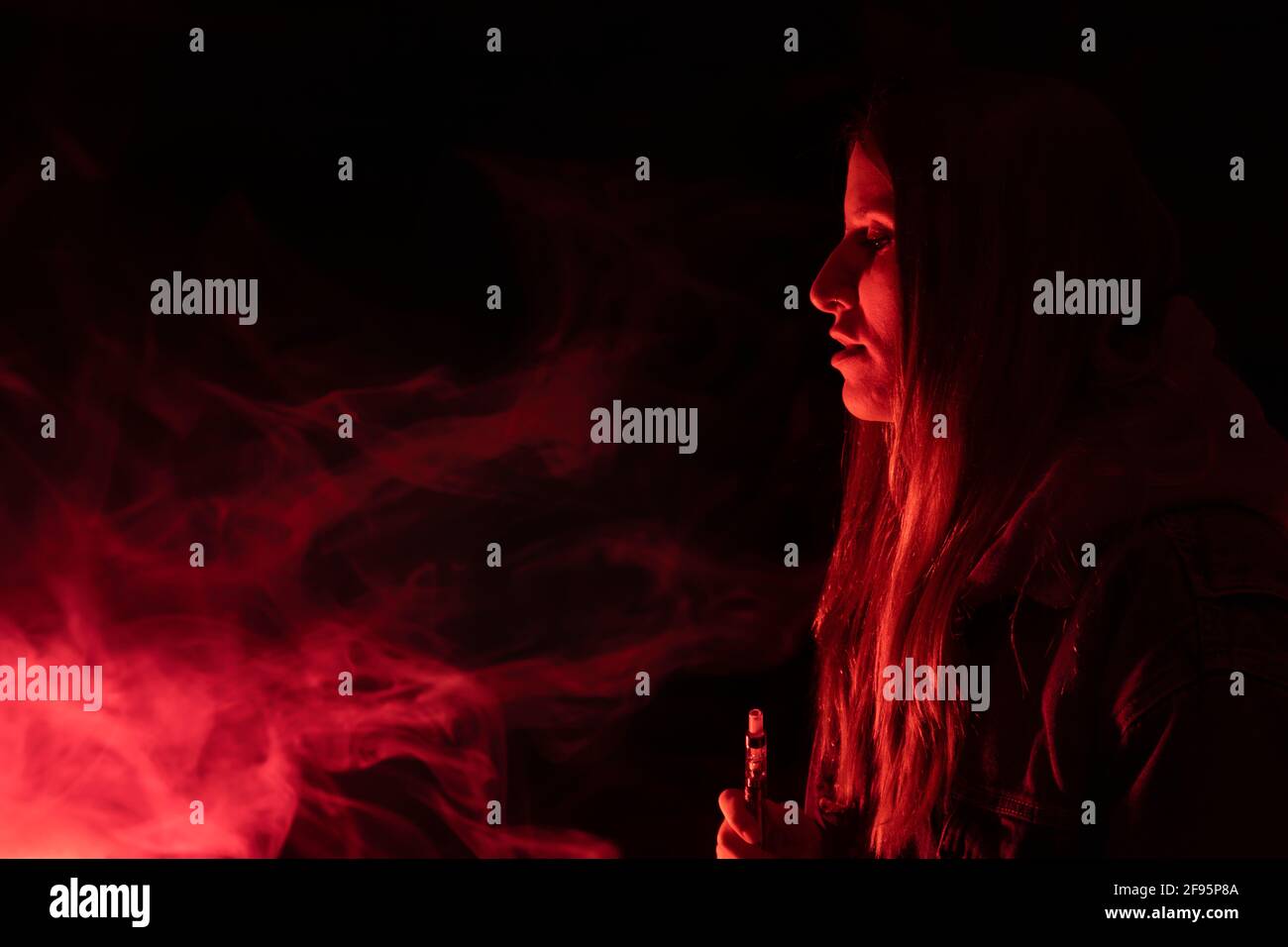 Vape Smoke Concept.Beautiful Frau vaper Rauchen in dunklem Hintergrund mit neon roten Lichtern.Party Club Lifestyle mit Copy Space. Stockfoto