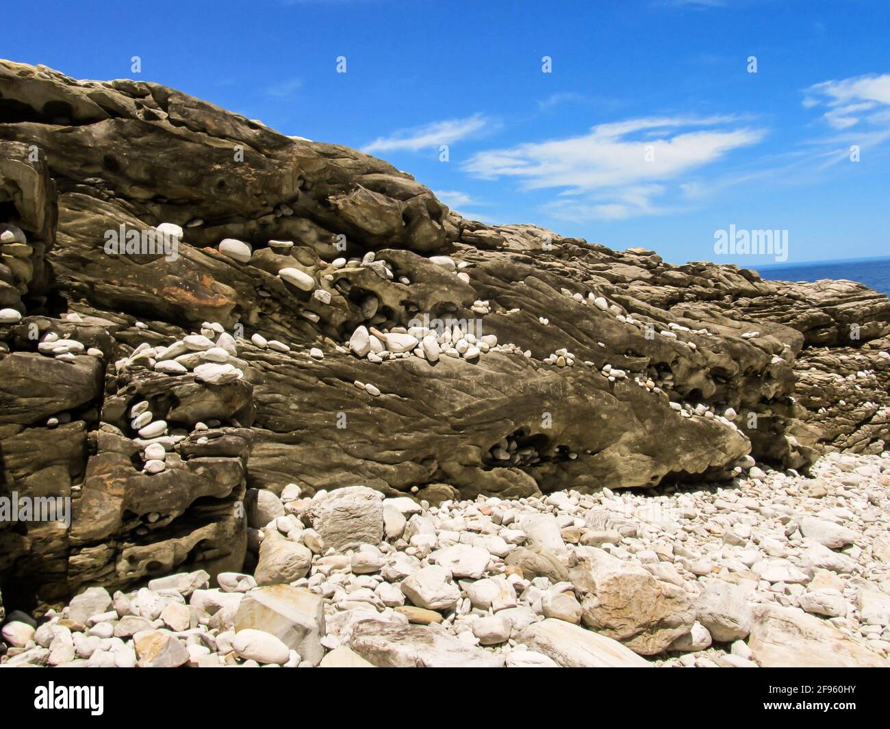 Weiße Kieselsteine verschiedener Formen und Größen, die entlang der Felsflossen der Tsitsikamma Coast, Garden Route National Park, Südafrika, verstreut sind Stockfoto