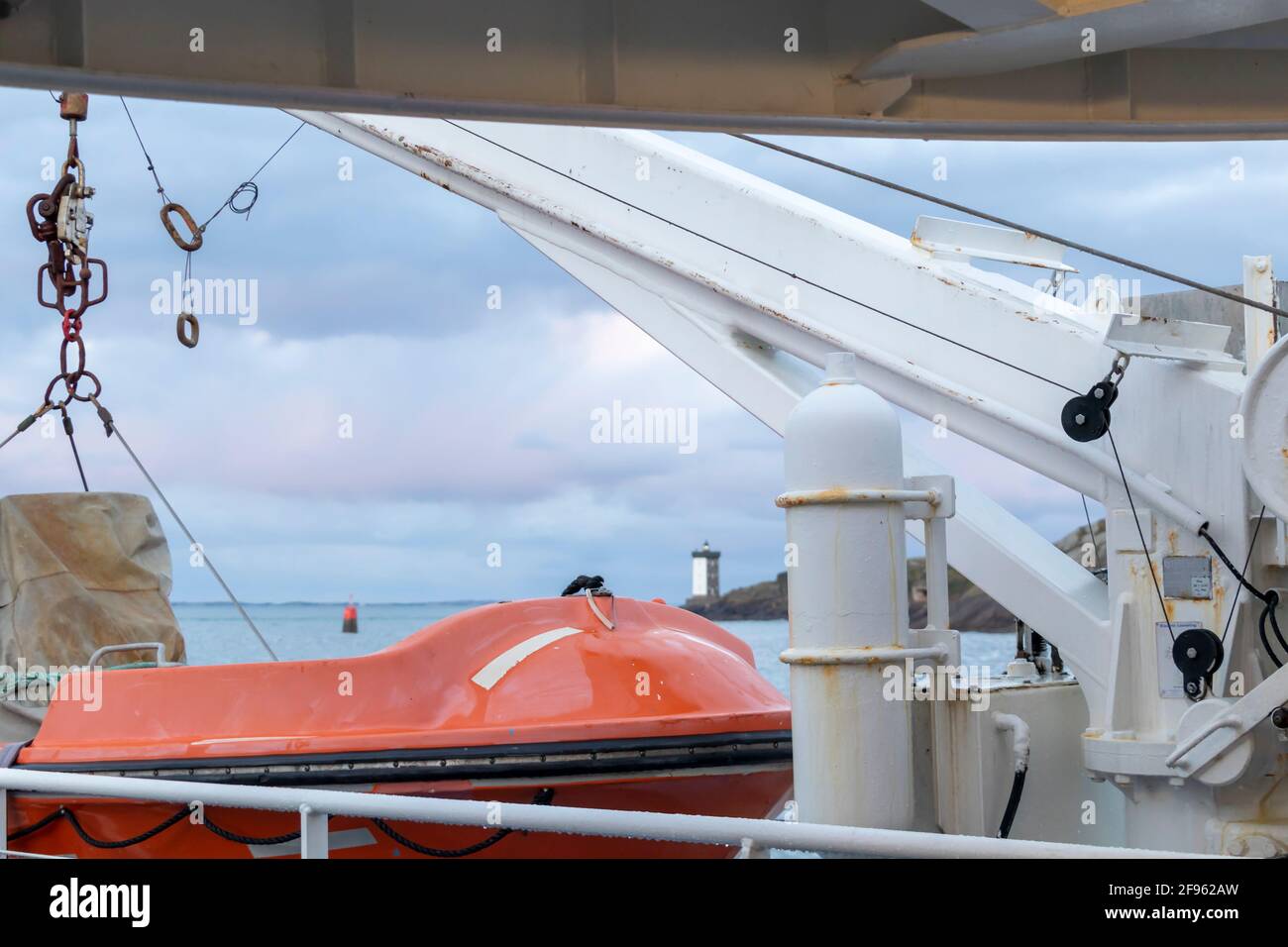 Transport und Sicherheit auf See. Rettungsinsel auf dem Fährdeck, orangefarbenes Rettungsboot bereit für die Evakuierung vom Bord, über einem blauen Meer an der Seite von hängend Stockfoto