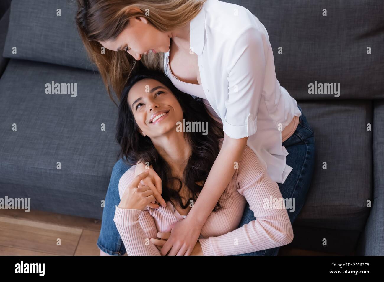 Fröhliche Lesben umarmen sich und schauen sich gegenseitig im Leben an Zimmer Stockfoto