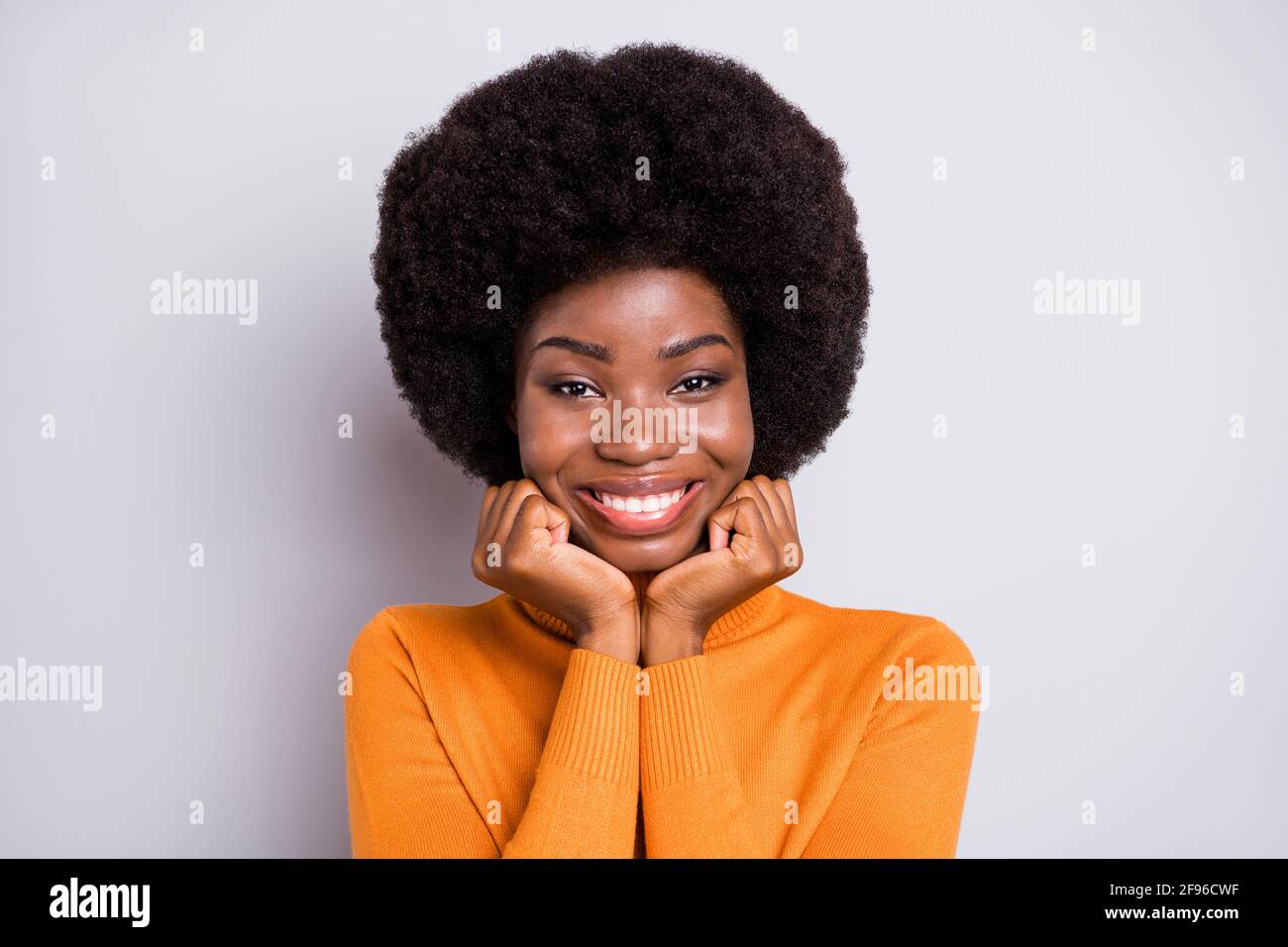 Foto von entzückenden schönen Dame Hände Wangen toothy Lächeln tragen Orange Rollkragen isoliert grauen Hintergrund Stockfoto