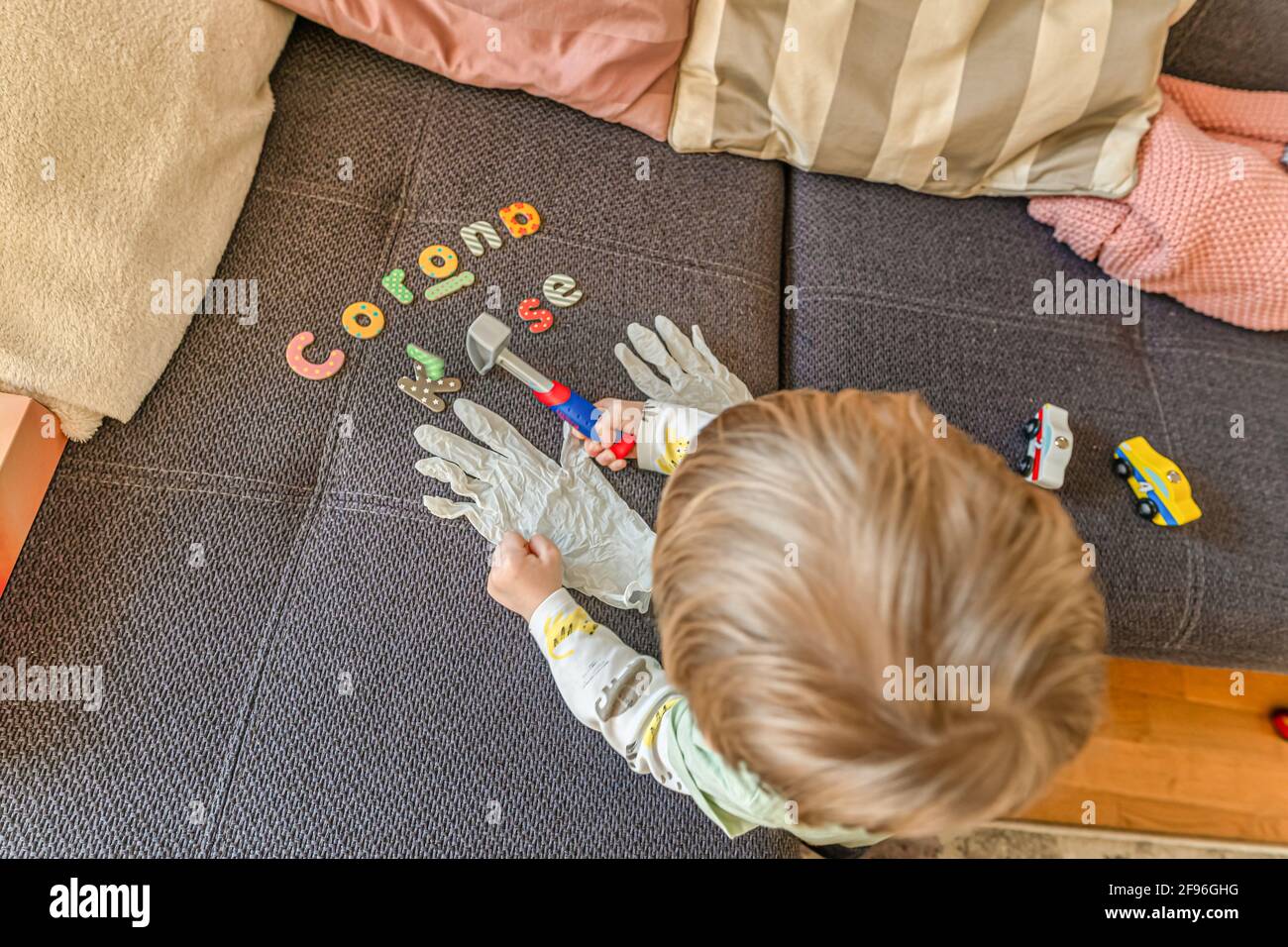 Tippte Buchstaben Corona Aufstieg in deutschen Worten ein, während ein kleiner Junge die Desinfektionshandschuhe ansah, während er sein Spiel unterbrach. Stockfoto