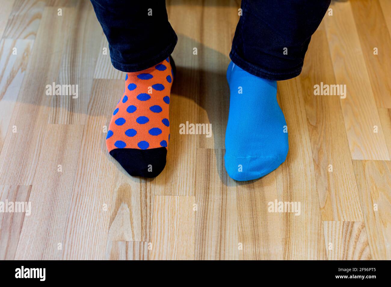 Down-Syndrom-Bewusstsein-Konzept. Mann mit verschiedenen Socken auf dem Holzboden stehend. Verschiedene Socken als Symbol des Daunen-Syndroms. Stockfoto