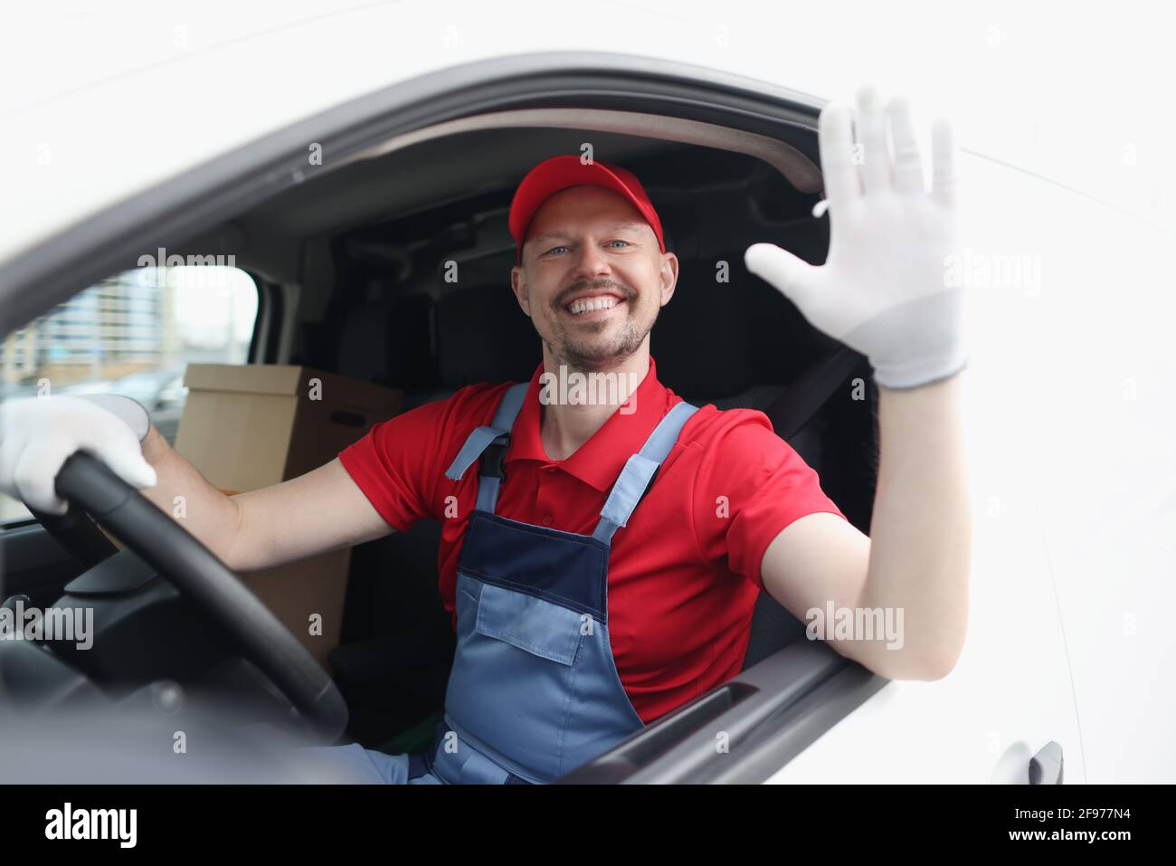 Lächelnder Kurierfahrer im Taxi winkt mit der Hand hinein Begrüßung Stockfoto