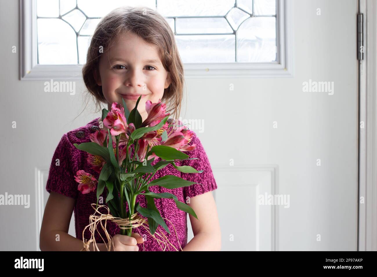 Junges Mädchen hält Bouquet von frischen rosa Alstroemerias Blumen, lächelnd und Blick auf die Kamera Stockfoto