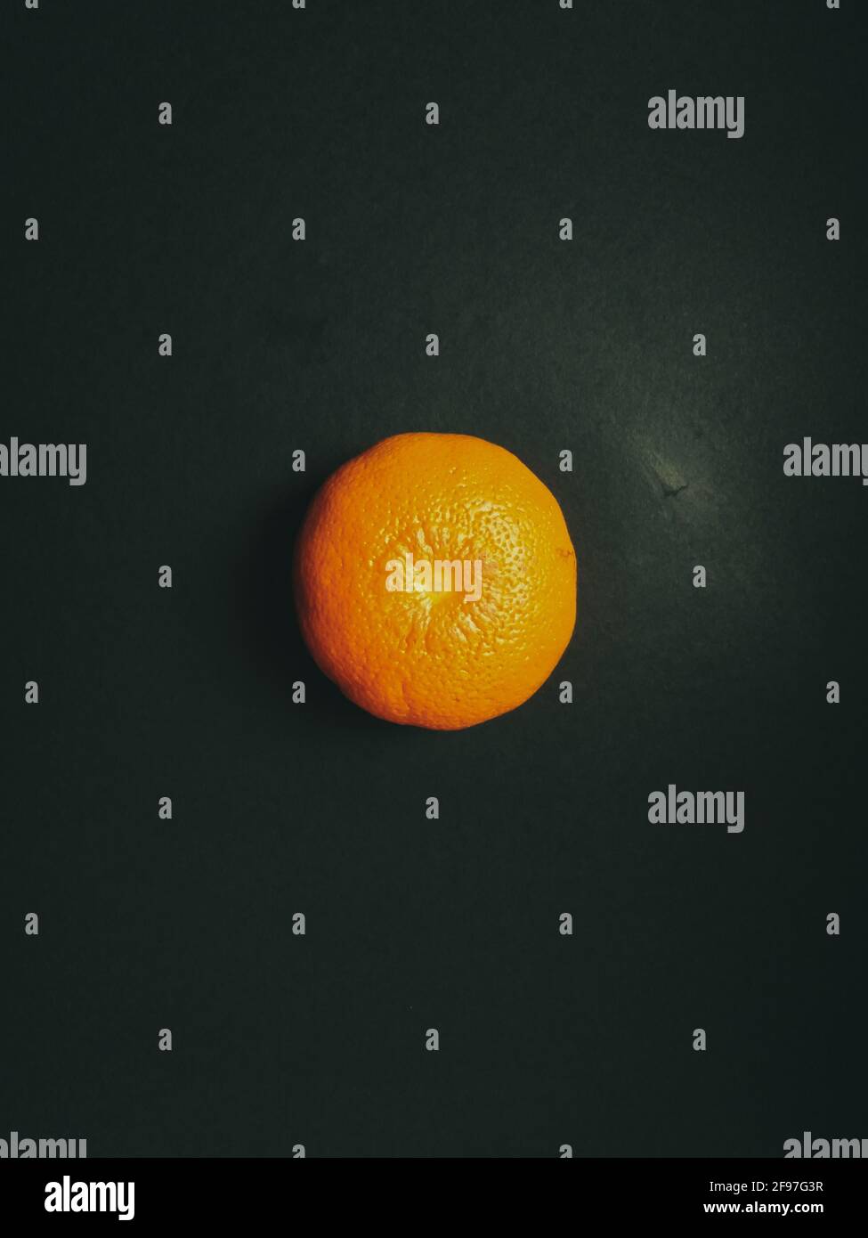 Vertikale Aufnahme einer frischen orangefarbenen Mandarine auf einem dunklen Grüne Oberfläche Stockfoto