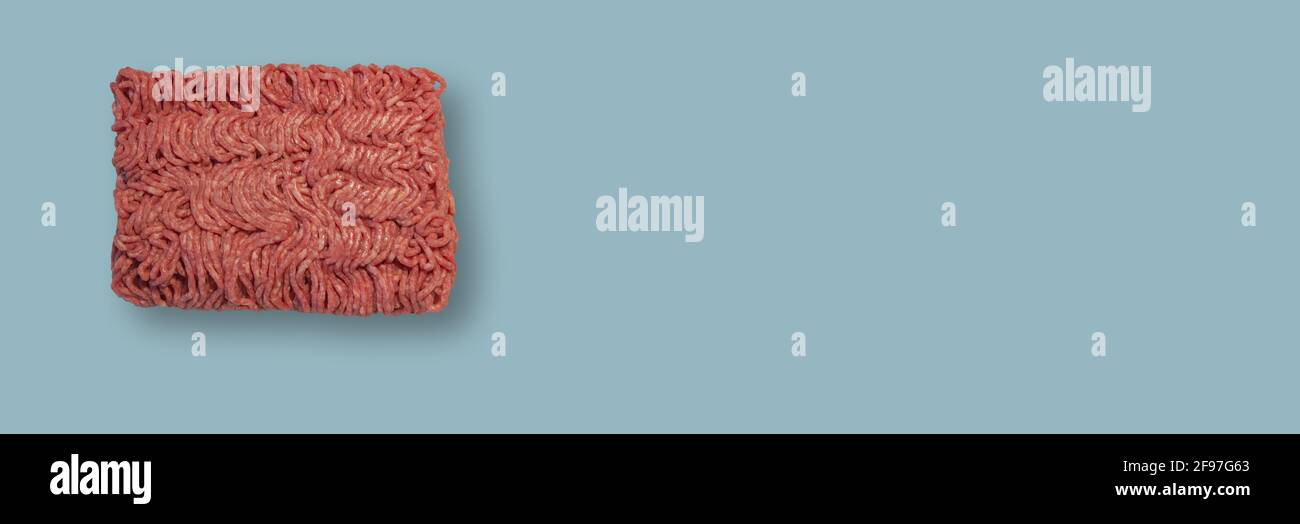Banner mit einem Ziegel aus rohem Hackfleisch auf hellblauem Hintergrund mit Kopierraum, Nahaufnahme, Details. Konzept gesunde Ernährung und nahrhafte Lebensmittel Stockfoto
