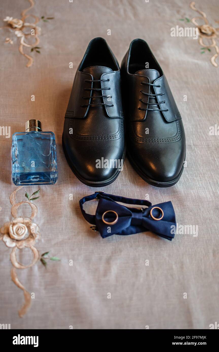 Accessoires für den Bräutigam. Schwarze Lederschuhe, goldene Eheringe, blaue Fliege, Parfüm Stockfoto