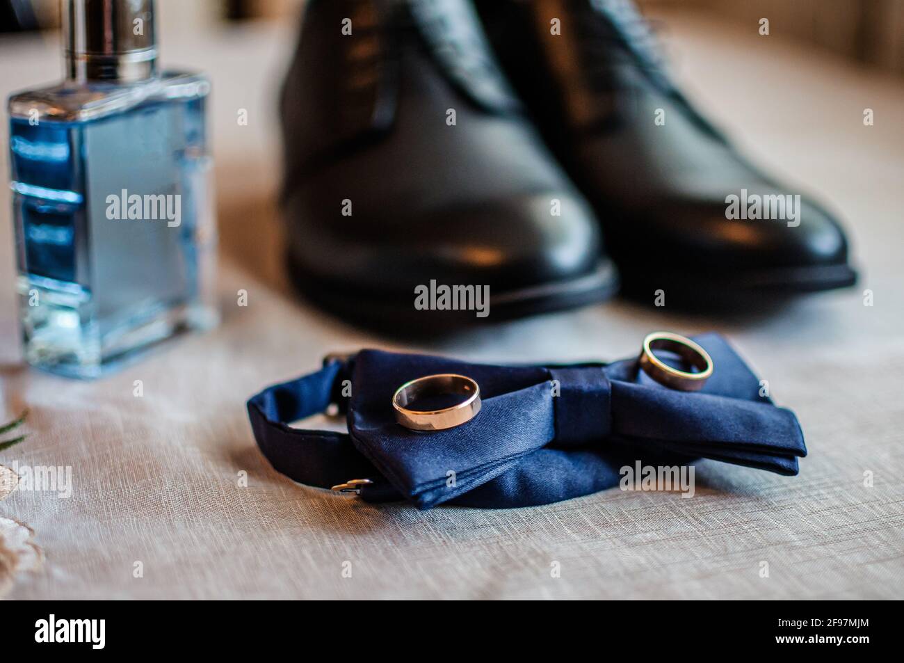 Accessoires für den Bräutigam. Schwarze Lederschuhe, goldene Eheringe, blaue Fliege, Parfüm Stockfoto