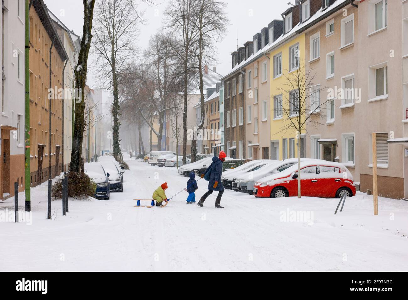 Essen, Nordrhein-Westfalen, Deutschland - Wintereinbruch im Ruhrgebiet, verschneite Wohnstraße in Holsterhausen, Mutter mit Kindern auf Schlitten auf der verschneiten Straße. Stockfoto