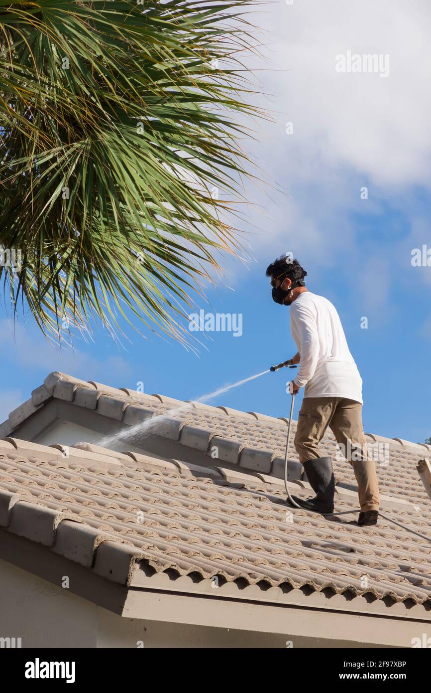 Mann macht waschen ein Fliesendach in Florida. Das Hochdruckspray entfernt Blätter, Zweige, Schmutz, Schmutz, Schlamm, Moos, Schimmelsporen, Flechten und Algen. Stockfoto