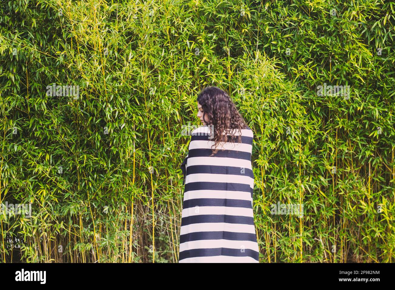Frau mit gestreifter Decke auf dem Feld gegen Bambusblätter bedeckt Stockfoto