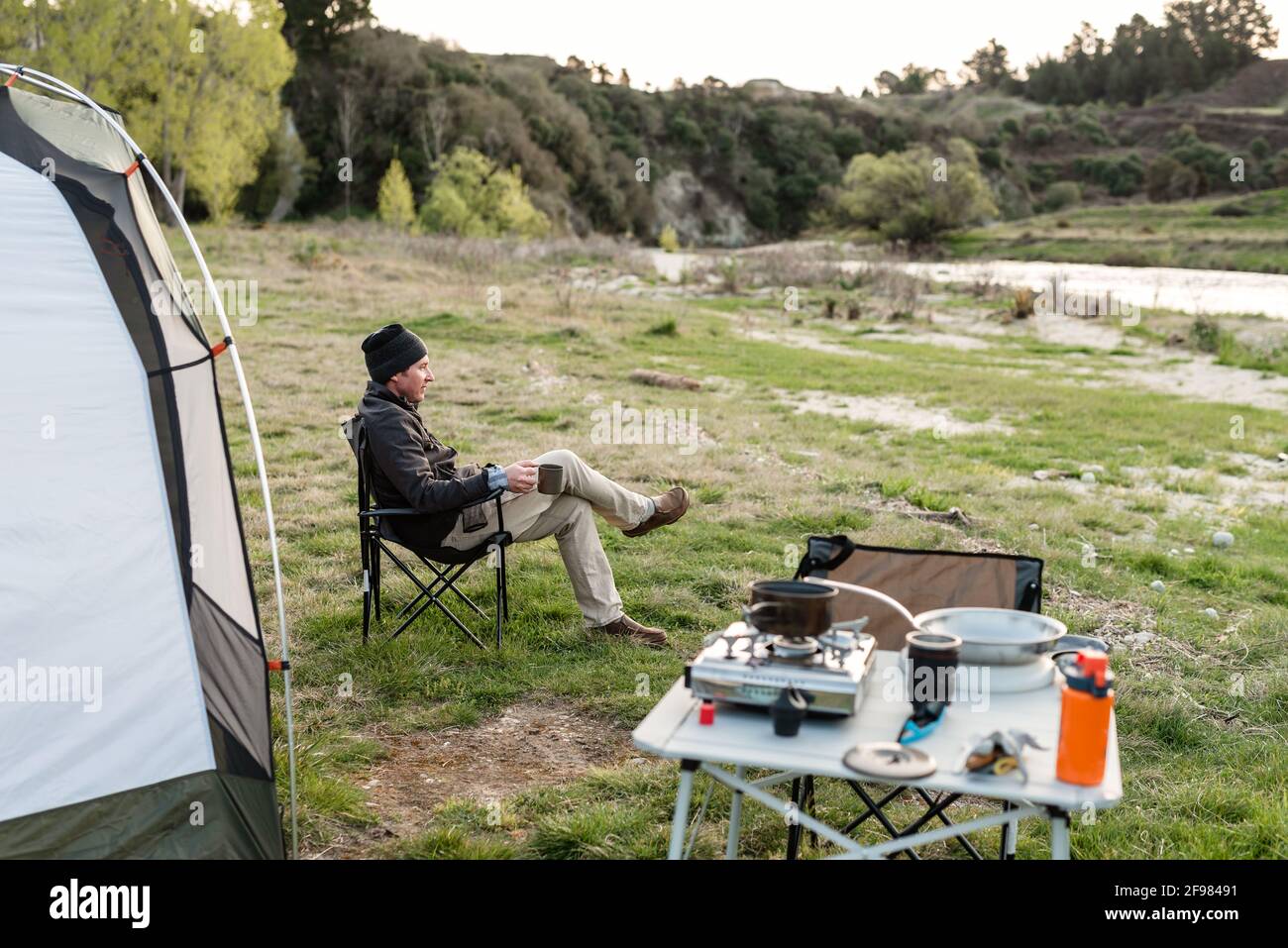 Mann, der in der Nähe des Zeltes im Lager in Neuseeland sitzt Stockfoto