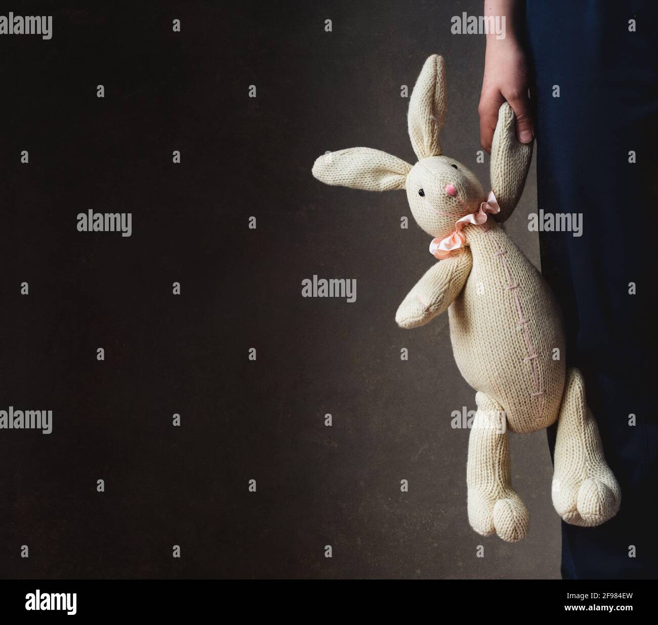 Zugeschnittenes Bild der Hand des Kindes, das ausgestopftes Kaninchen gegen Dunkelheit hält Wand Stockfoto