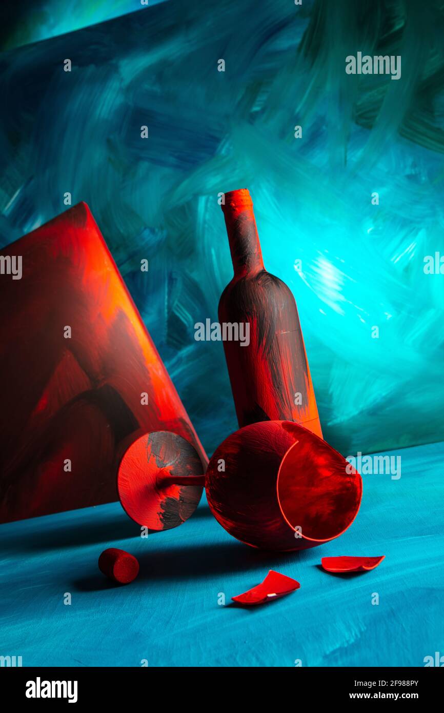 Rot bemalte Weinflasche und Weinglas auf blauem Hintergrund. Stockfoto