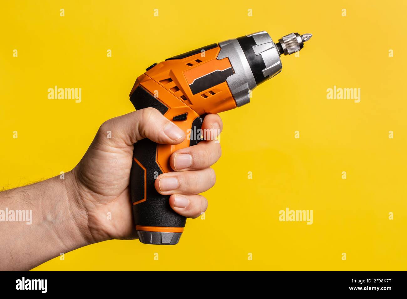 Hand eines unbekannten Mannes mit elektrischem Schraubendreher - männlicher Halt Arbeit Handwerk Werkzeug auf hellgelben Hintergrund - Reparatur Renovierung Elektrogeräte Stockfoto