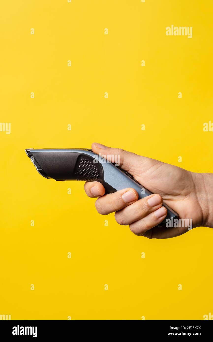 Nahaufnahme eines unbekannten kaukasischen Mannes mit Elektroantrieb Bartschneider schnurloser Haarschneider vor modernem Gelb Hintergrund Stockfoto