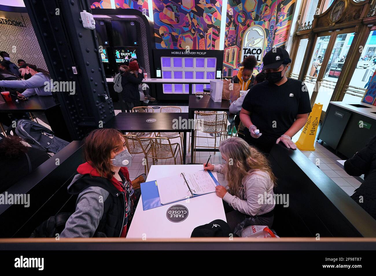 New York, USA. April 2021. Eine Kundin registriert ihre Kontaktinformationen, nachdem sie ihre Temperatur in Taco Bells neu eröffnetem „Digital Only“-Cantina-Restaurant an der 7th Avenue am Times Square, New York, NY, am 16. April 2021, eingenommen hat. Die Kunden haben Zugriff auf zehn Touchscreen-Menüs, über die sie ihre Lebensmittelbestellungen mit möglichst geringem Kontakt mit Menschen aufgeben und bezahlen können. Die Kunden lassen sich bei der Eingabe die Temperatur überprüfen und werden gebeten, sich für die Kontaktverfolgung in einem Buch zu registrieren. (Foto von Anthony Behar/Sipa USA) Quelle: SIPA USA/Alamy Live News Stockfoto