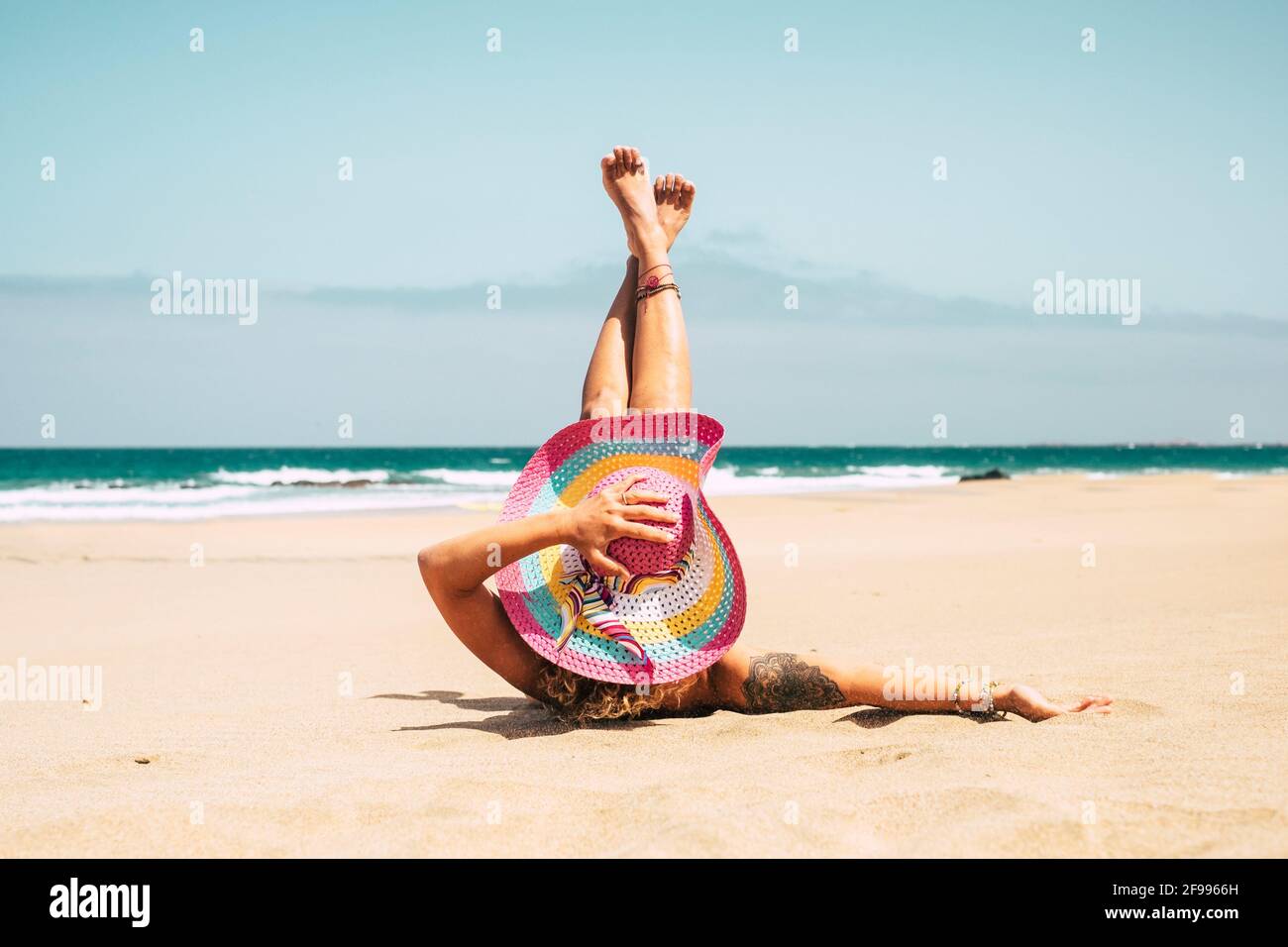 Frau mit bunten Hut genießen den Strand auf dem liegen Sand im Sommerurlaub  Urlaub Reise Lifestyle - junge Frau kaukasische Menschen nehmen ein  Sonnenbad allein mit blauem Ozean in Hintergrund Stockfotografie - Alamy