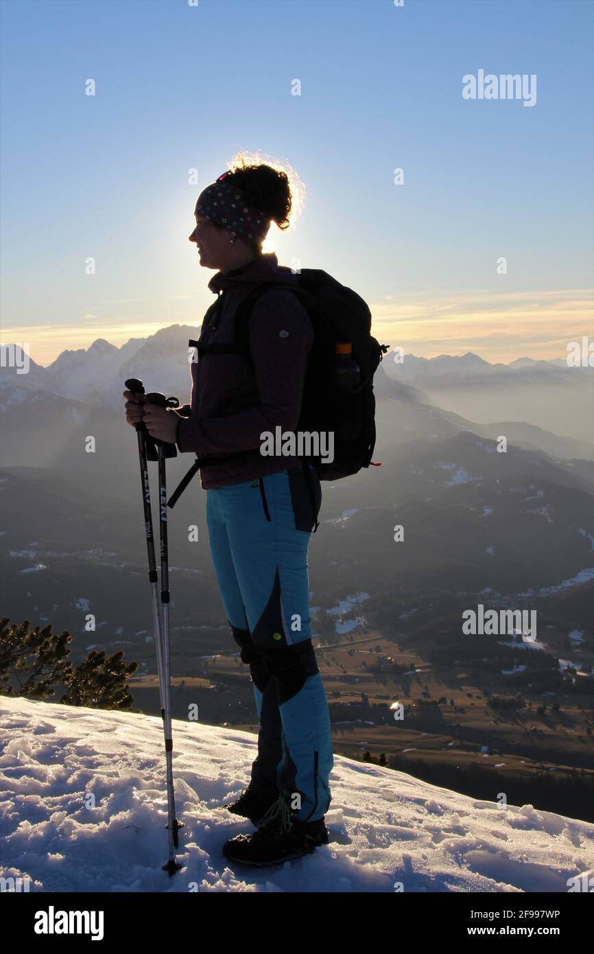 Winterwanderung zum Signalkopf (1895 Meter) mit Blick auf den Wettersteingebirge, Zugspitze, junge Frau steht bei Sonnenuntergang auf dem Gipfelgrat, Europa, Deutschland, Bayern, Oberbayern, Isartal, Krün Stockfoto