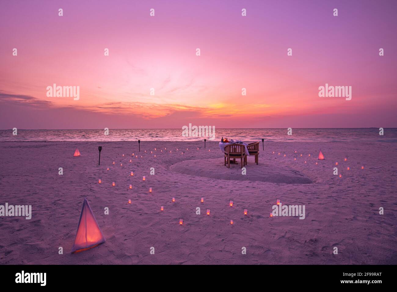 Tolles romantisches Abendessen am Strand auf der Holzterrasse mit Kerzen unter dem Sonnenuntergangshimmel. Romantik und Liebe, Luxus-Destination Dining, exotische Tisch-Setup Stockfoto