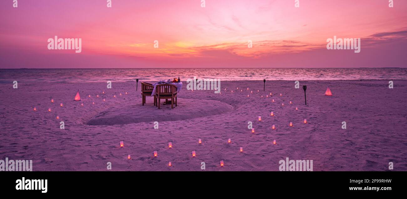 Tolles romantisches Abendessen am Strand auf der Holzterrasse mit Kerzen unter dem Sonnenuntergangshimmel. Romantik und Liebe, Luxus-Destination Dining, exotische Tisch-Setup Stockfoto