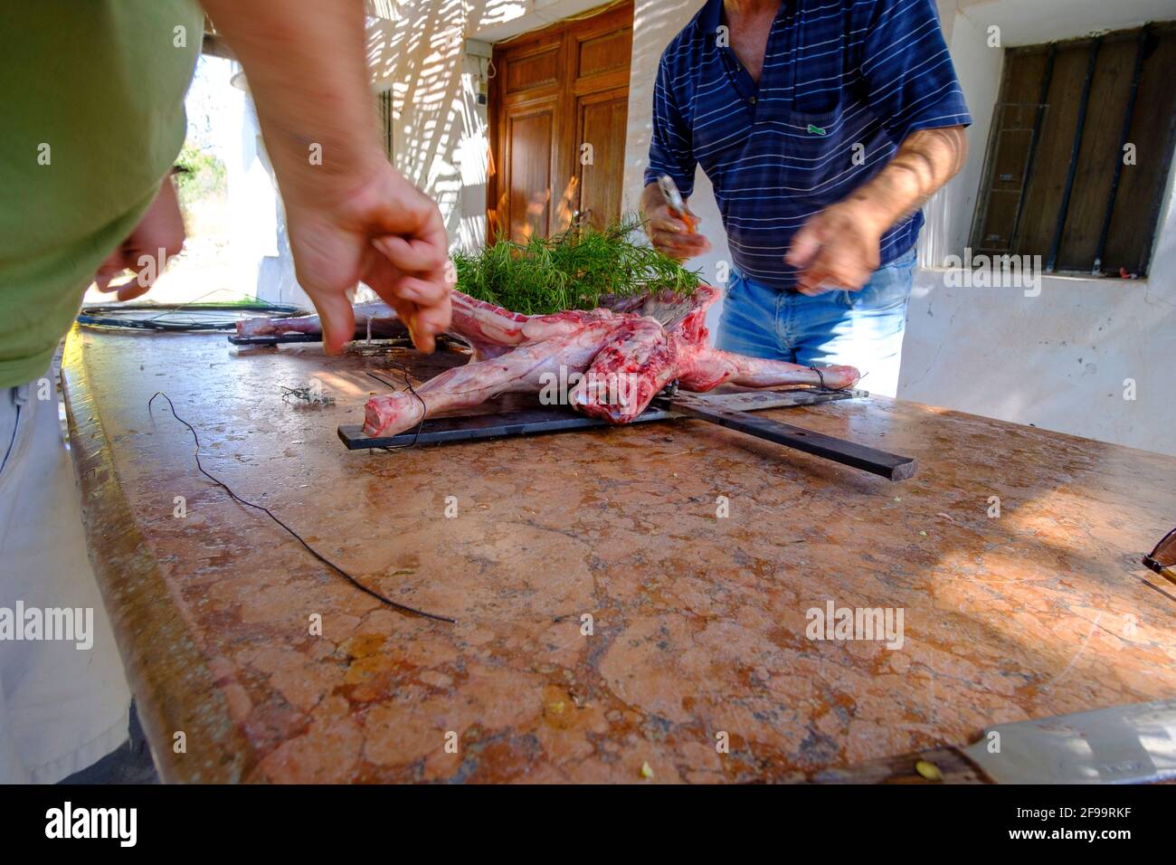 Zwei Männer bereiten in Altea La Vella, Alicante, Spanien, das ganze Lamm-Asado zu und binden es an das Eisenkreuz Stockfoto