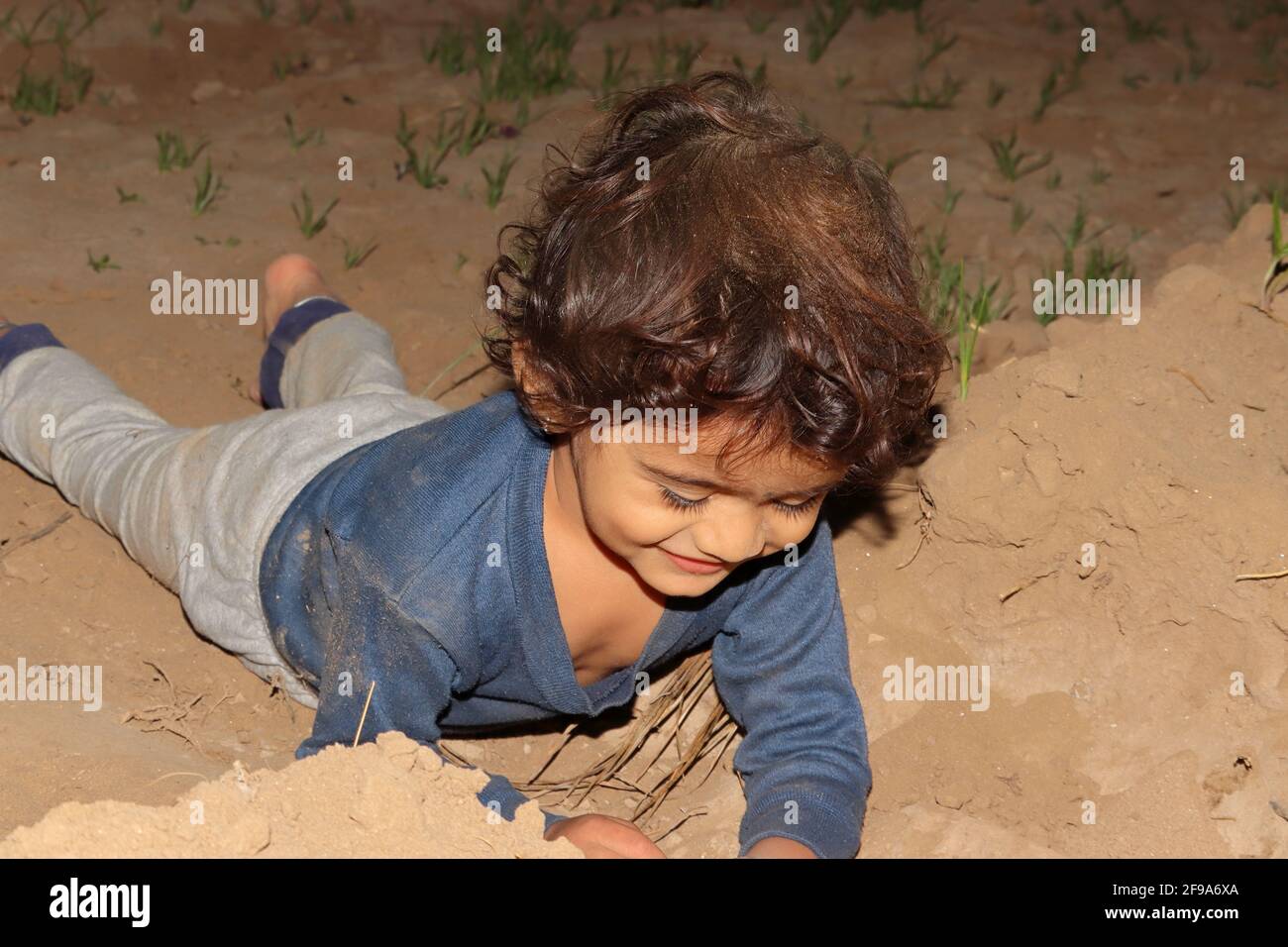 Nahaufnahme eines indischen Kindes, das mit Erde spielt und auf dem Feld auf dem Boden liegt, Konzept bis zur Kindheit. Stockfoto