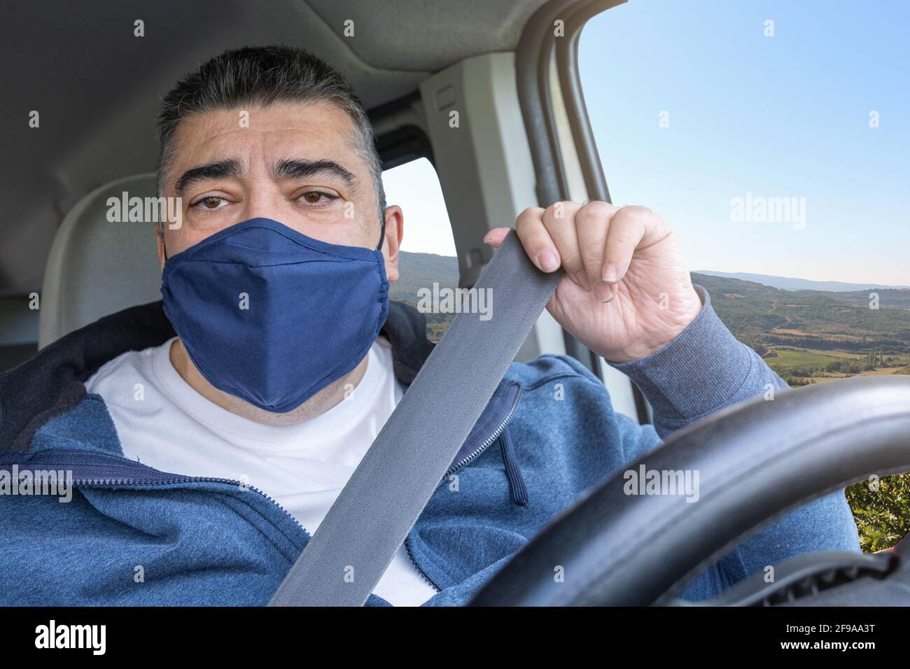Mann mittleren Alters mit blauer Gesichtsmaske, der sein Auto aufsetzt Sicherheitsgurt vor der Fahrt zur Arbeit oder zu Hause Konzept mit selektivem Fokus Stockfoto