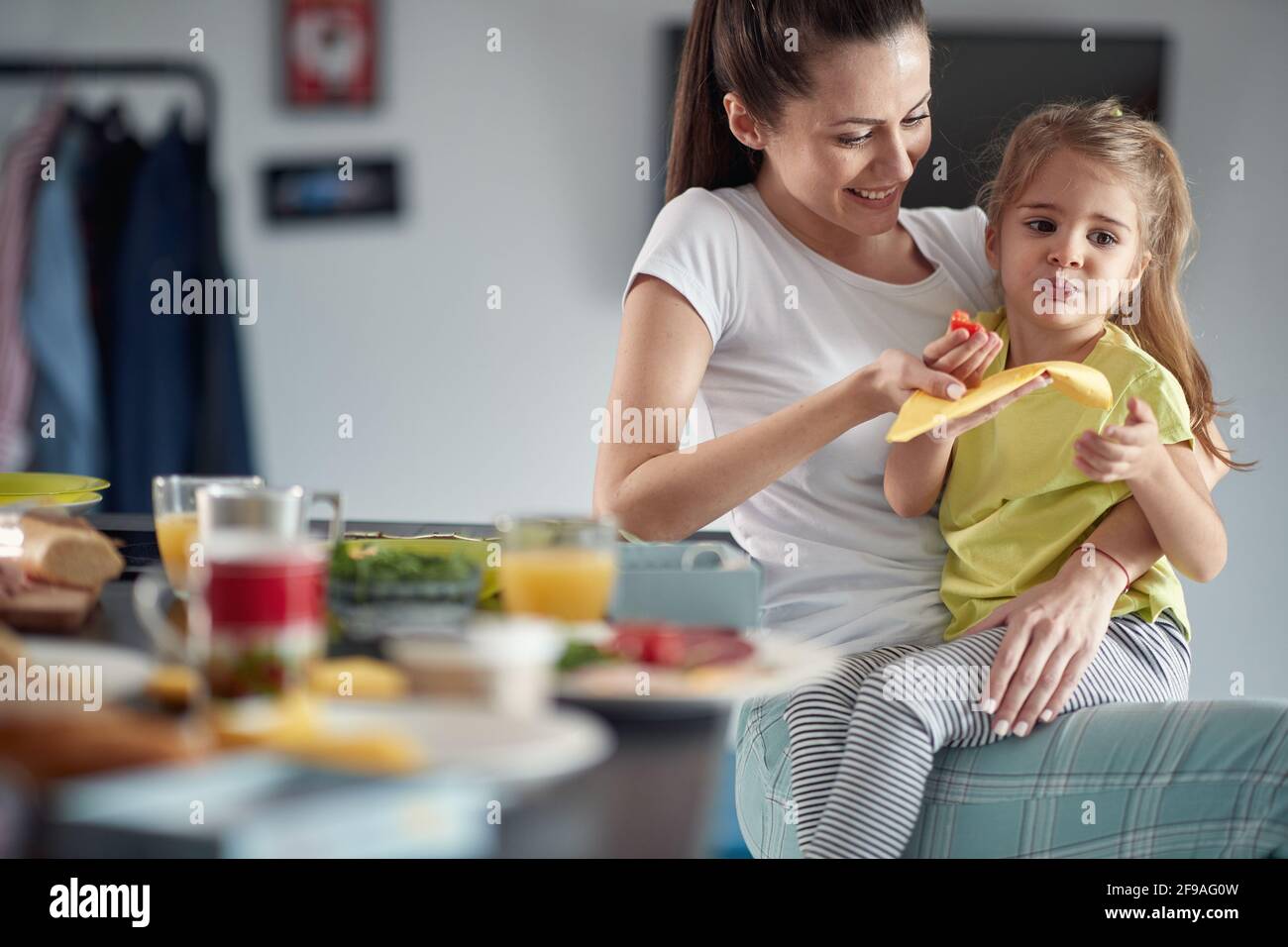 Ein kleines Mädchen genießt ein Frühstück in entspannter Atmosphäre zu Hause, während sie auf dem Schoß der Mutter sitzt. Familie, Frühstück, zusammen, Zuhause Stockfoto