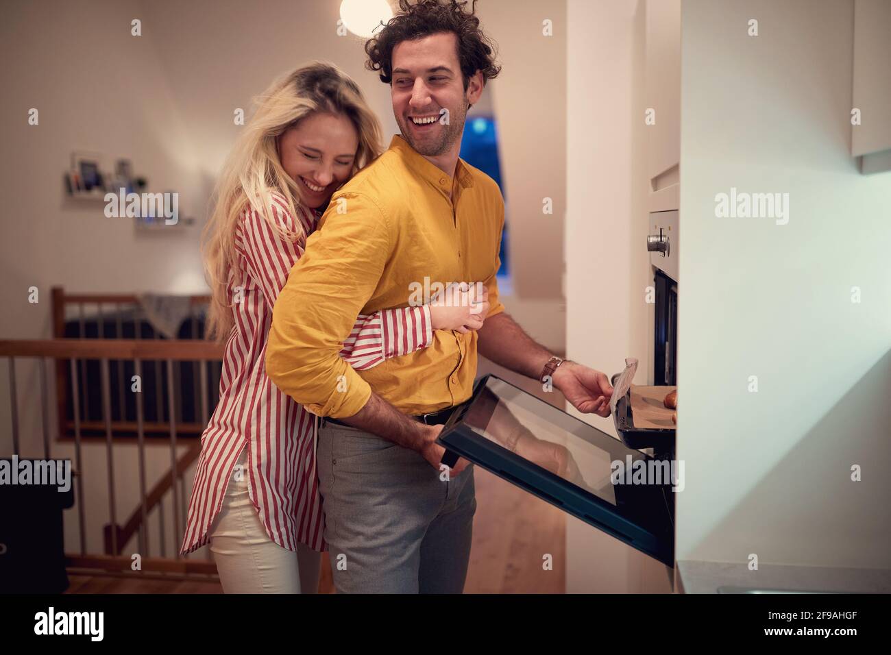 Junge Erwachsene kaukasische Frau umarmt ihren Mann, der kocht. valentine, romantisch, Zweisamkeit Stockfoto